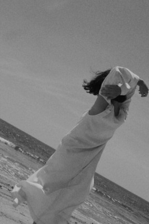 Back of a person at the shore arms wrapped overhead wearing Duster Dress by Eckhaus Latta - in a black and white photograph