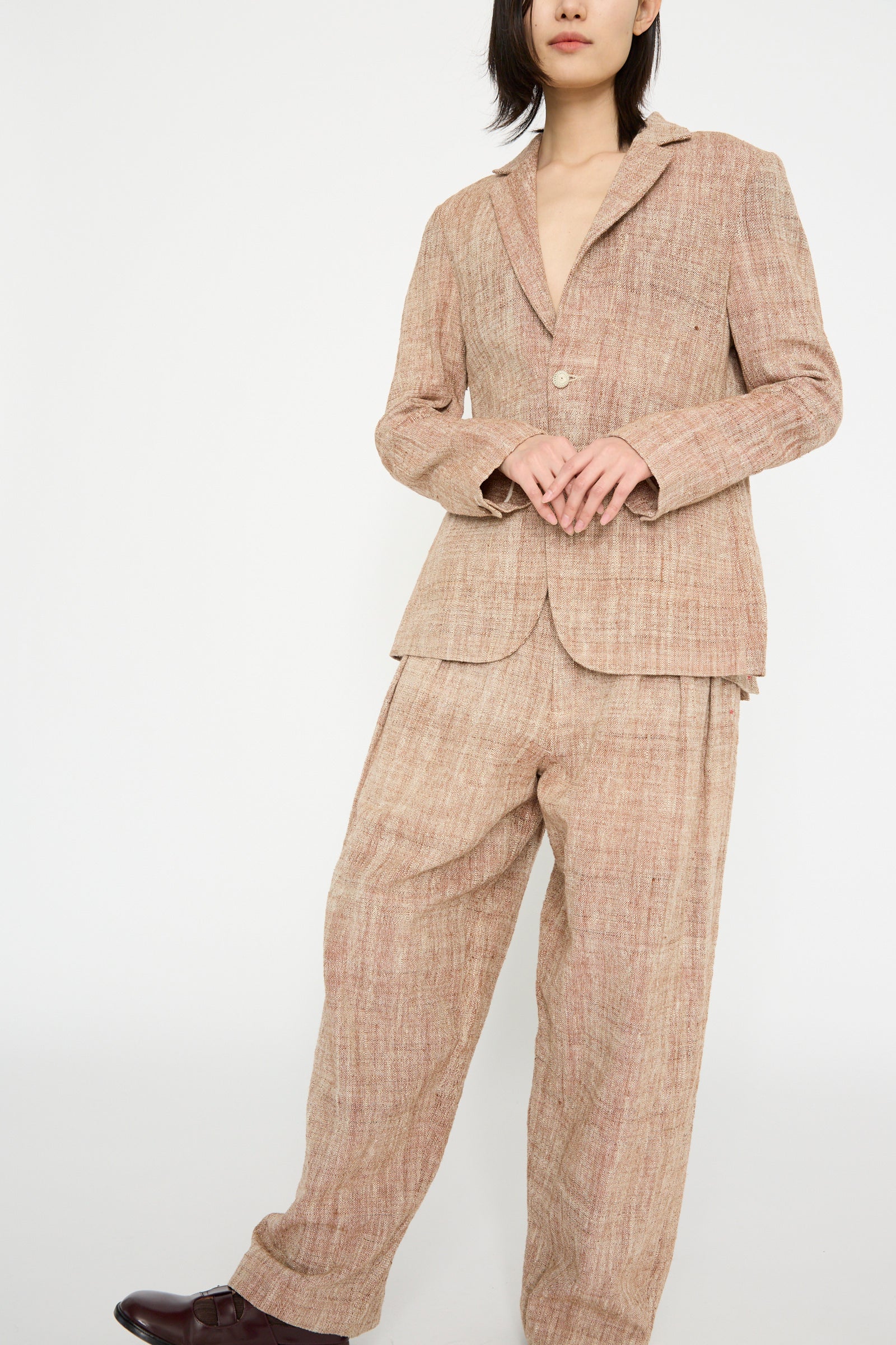 A person in an 11.11 Cotton Blazer in burnt umber with a notched collar and relaxed fit, paired with wide-leg trousers, stands against a plain background.