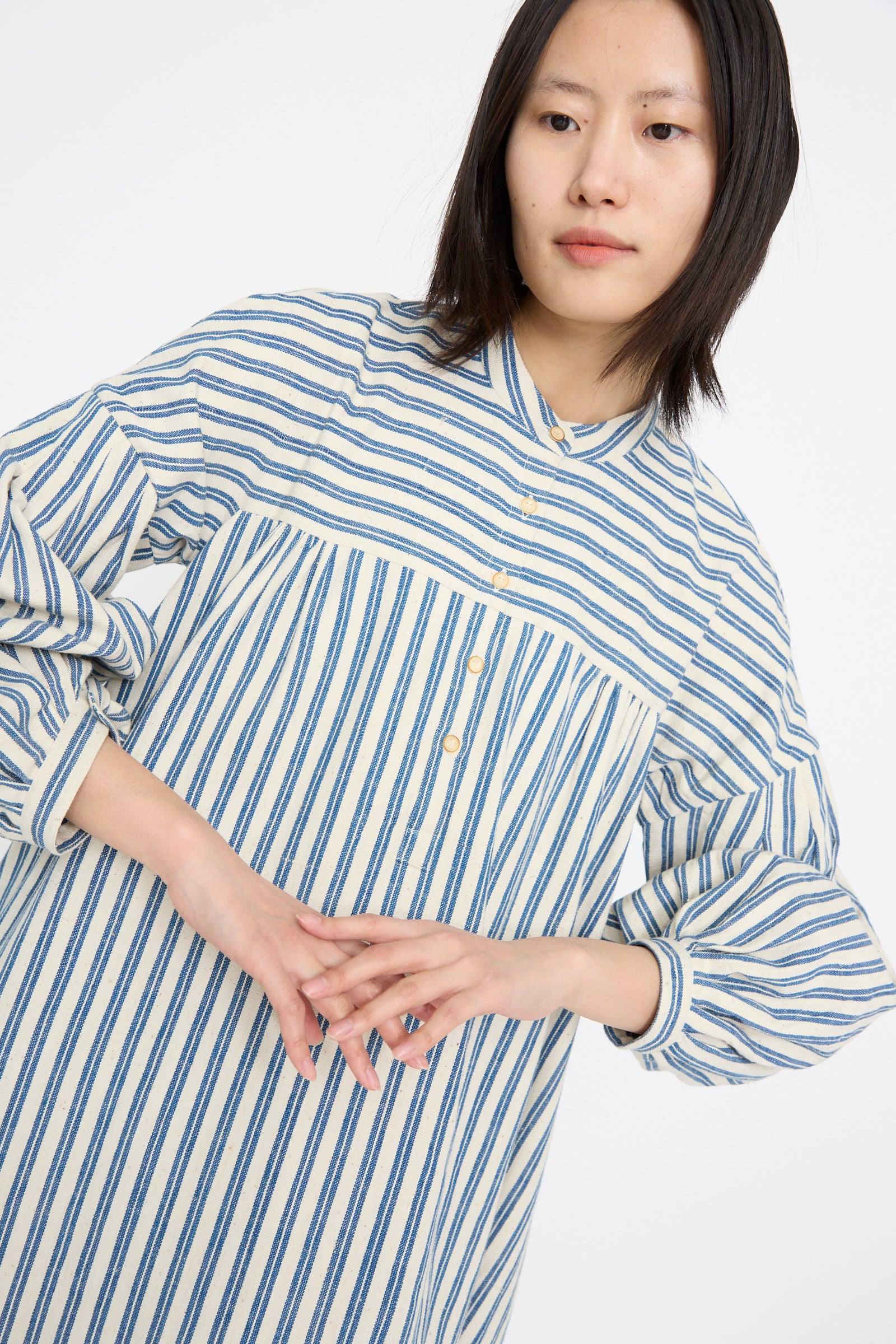 A person poses gracefully against a plain backdrop wearing the 11.11 Cotton Gurue Dress in Medium Indigo Stripe with an A-line silhouette.