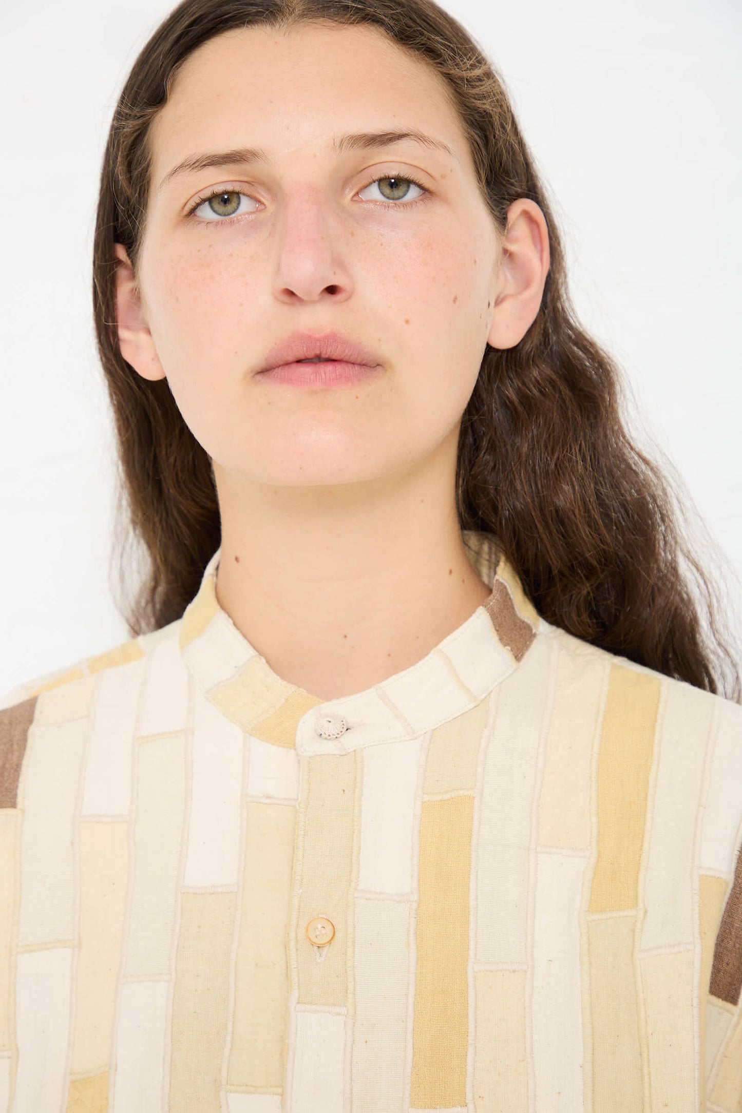 A person with long, wavy hair wearing the Cotton Patchwork Statement Shirt in Shades of Ecru by 11.11 looks directly at the camera against a plain background.