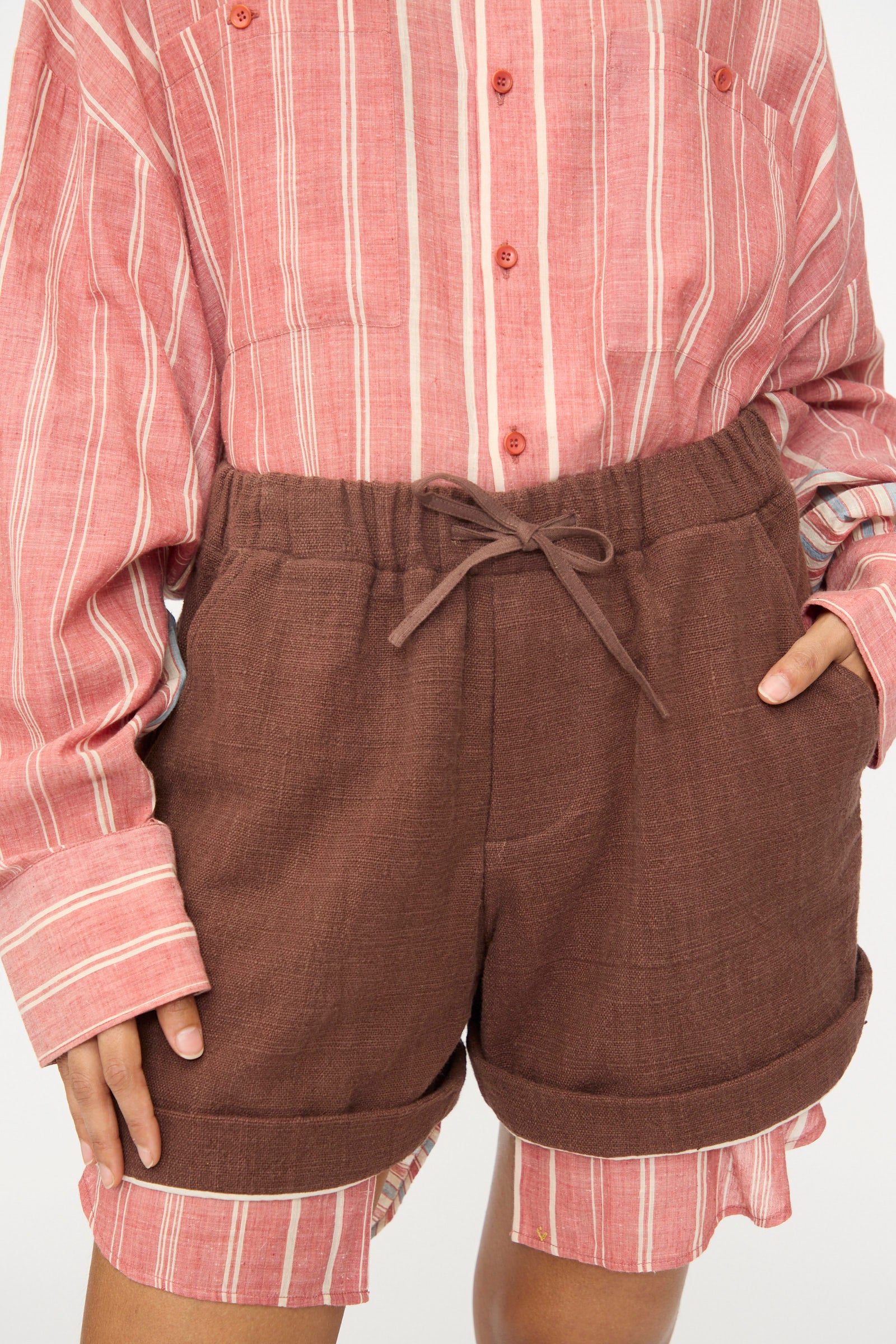 Model wearing the 11.11 Cotton Short in Dark Brown with a relaxed fit, drawstring waist, and rolled hems, shown from mid-torso to mid-thigh.