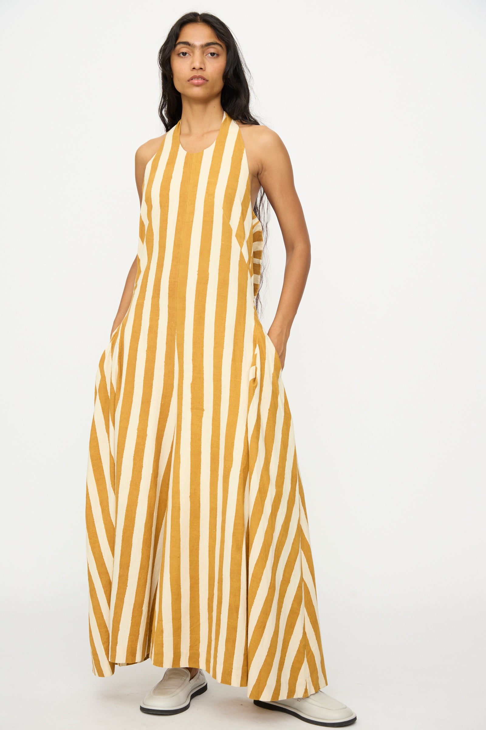 A person wears the 11.11 Cotton Stripe Jumpsuit in Mustard Yellow—a sleeveless, wide-leg, handwoven cotton piece with vertical yellow and white stripes—standing against a plain white background.
