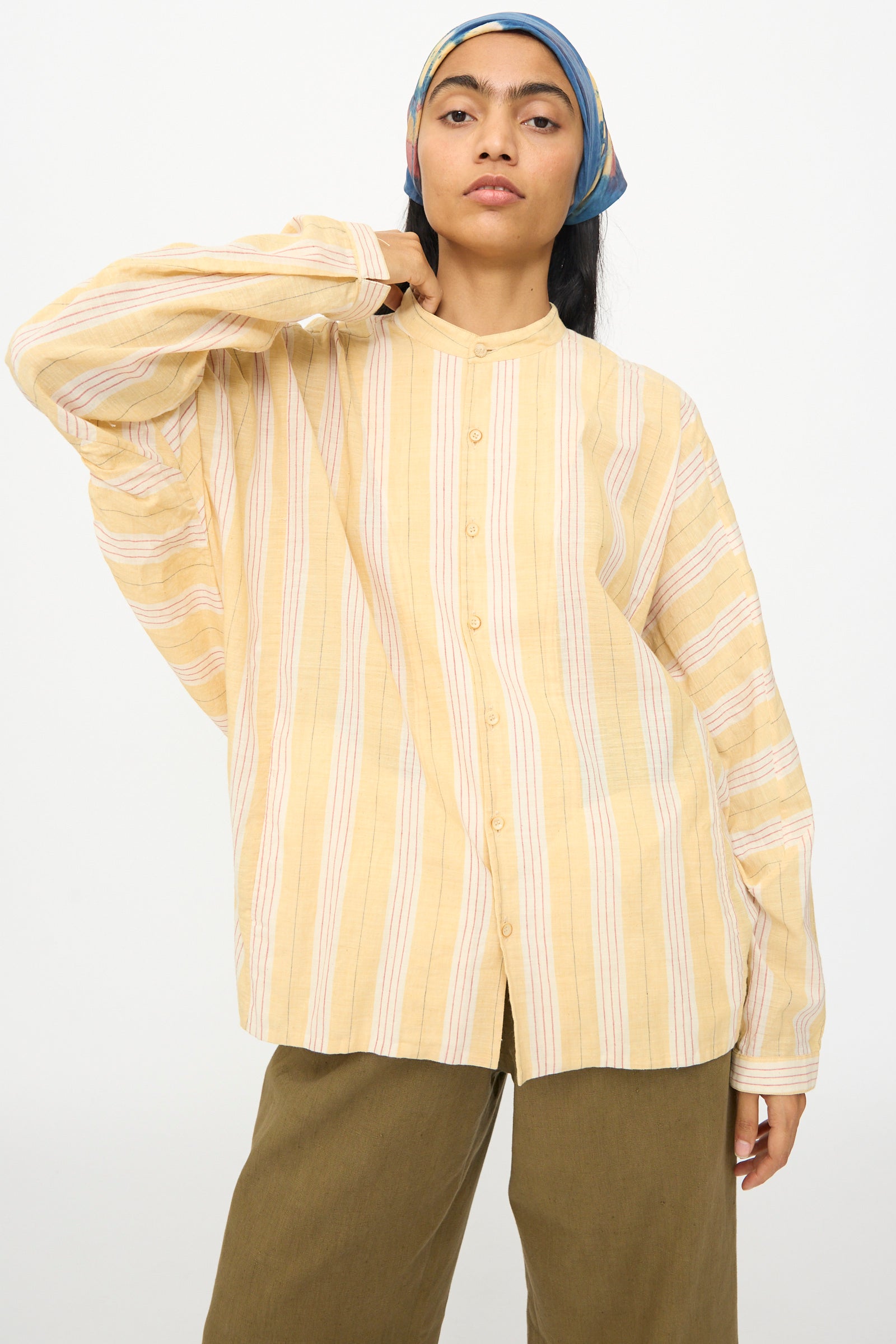 A person wears the 11.11 Cotton Stripe Shirt in Mango Yellow with a band collar, paired with olive green pants and a blue patterned headscarf, standing against a plain background.