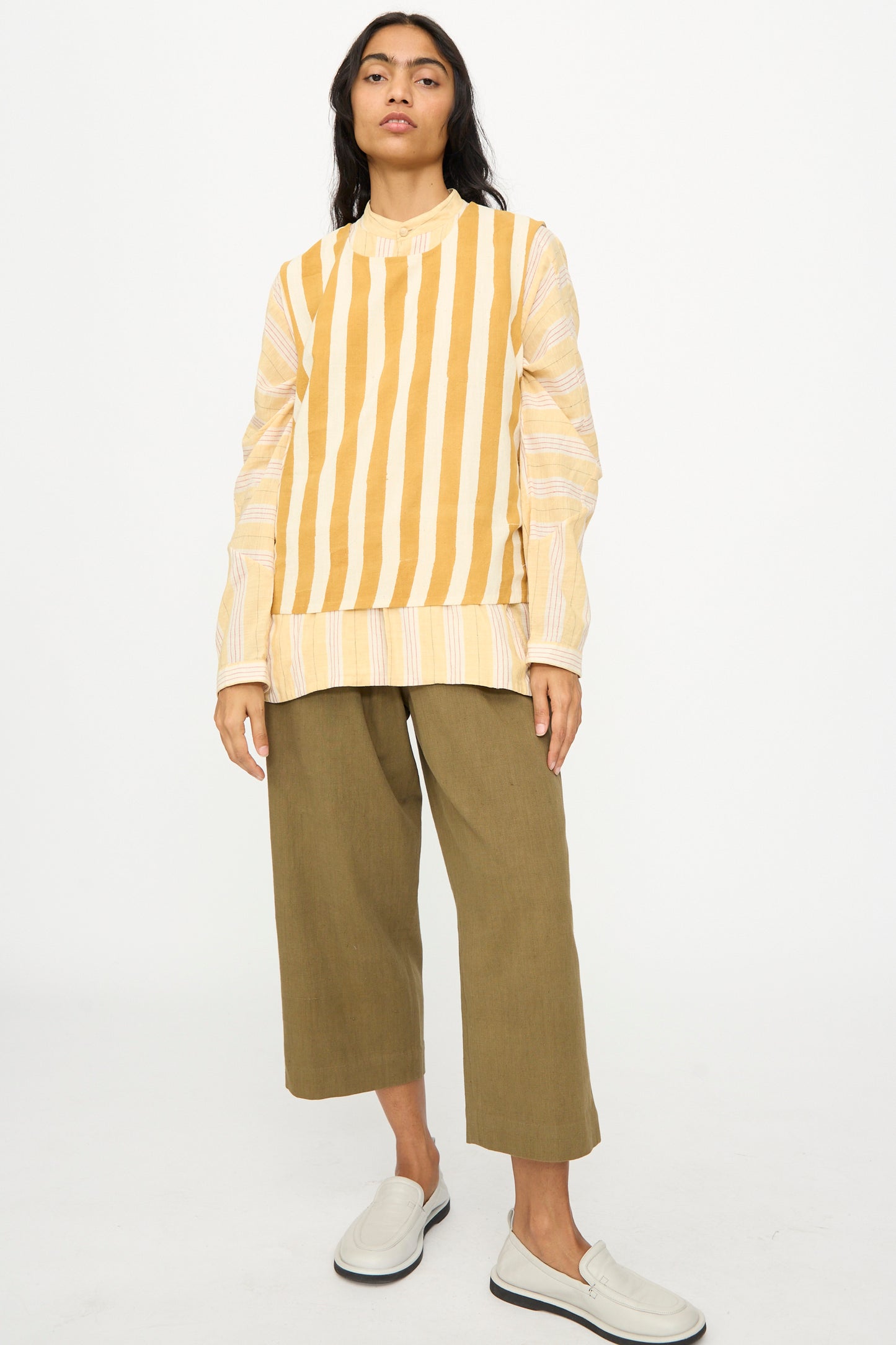 A person faces forward against a white background, wearing the 11.11 Cotton Stripe Top in Mustard Yellow, paired with olive cropped pants and white slip-on shoes.
