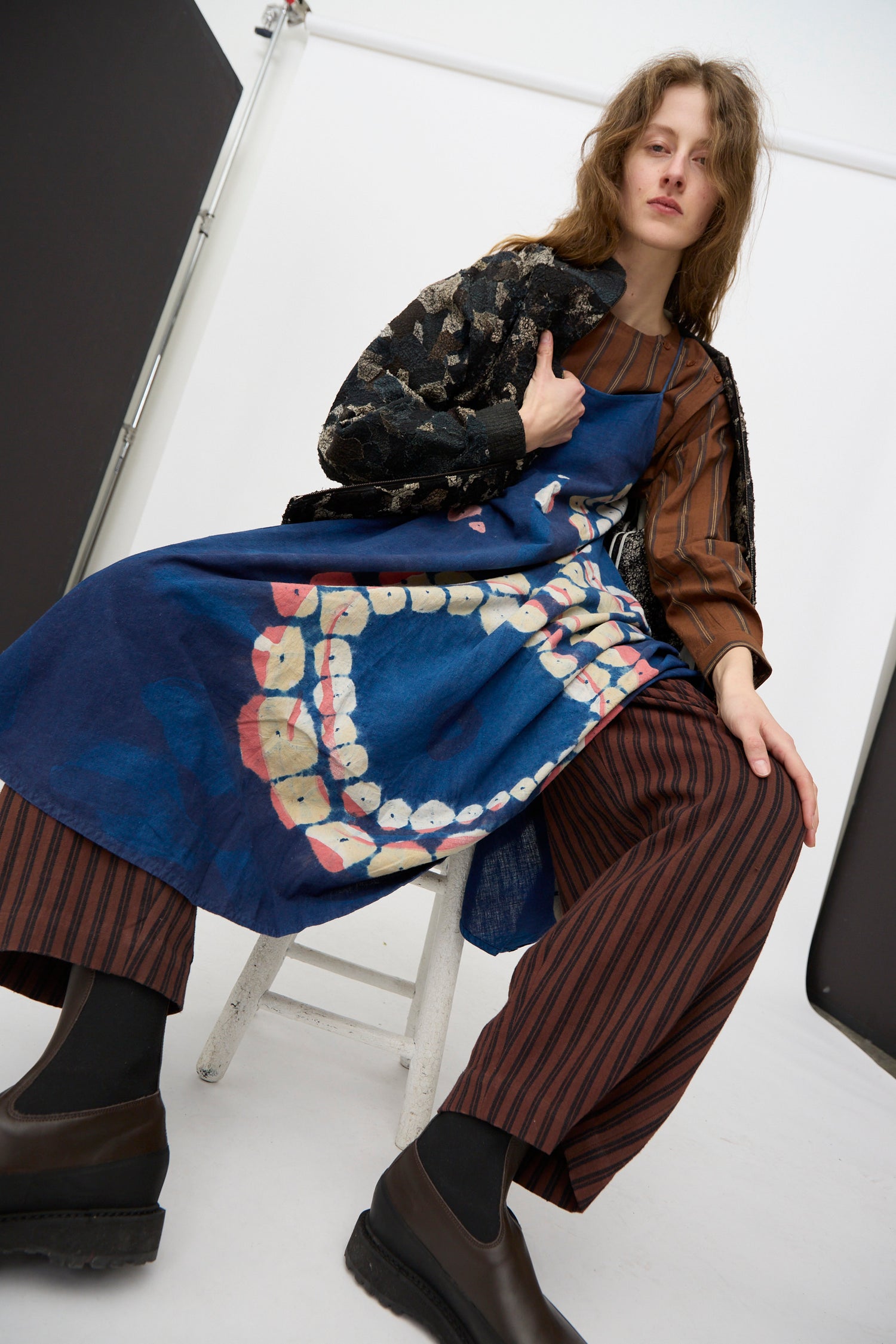A person wearing pieces of 11.11 clothing sitting on a stool against a white background.