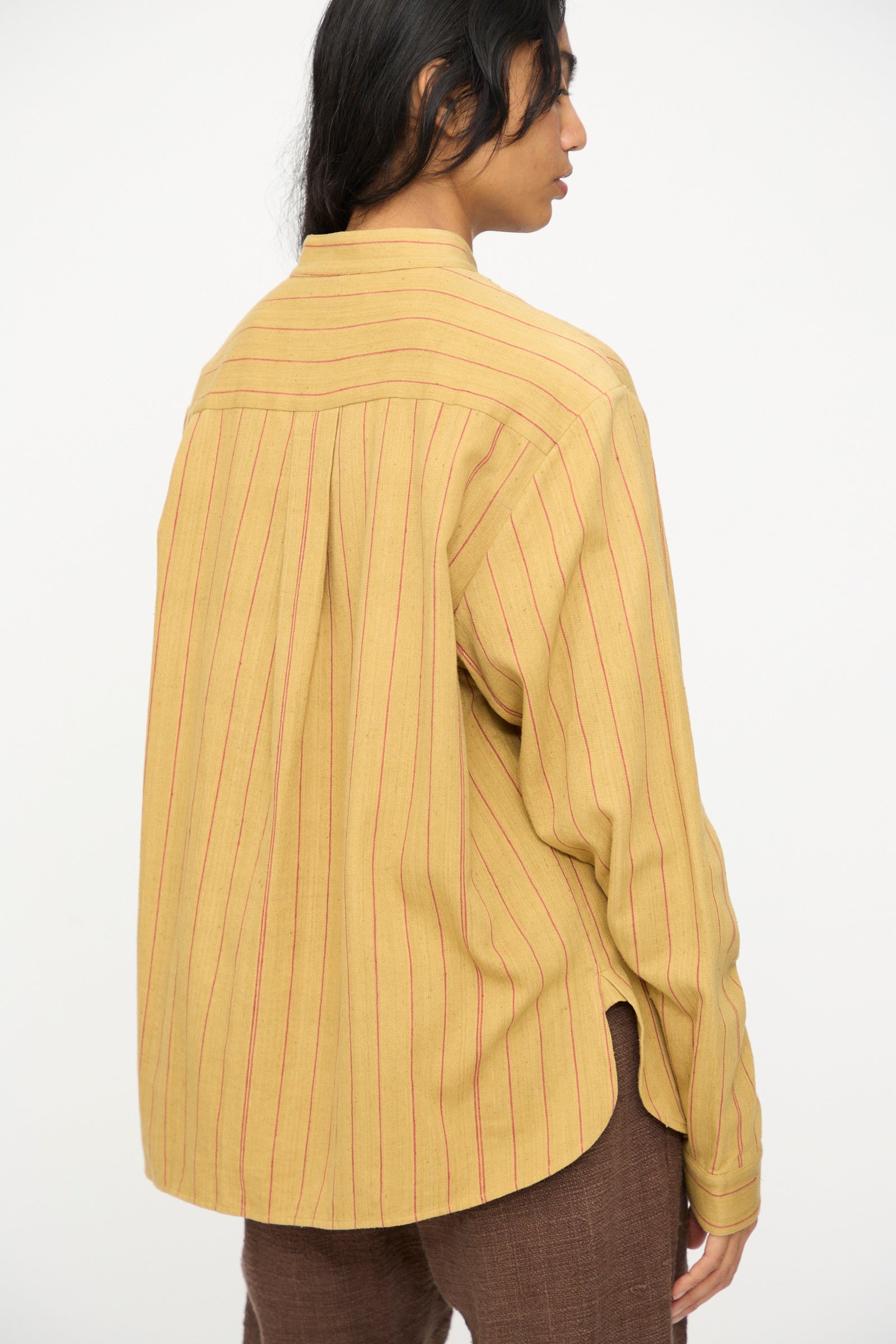 A person wears the 11.11 Lovers Shirt in Ochre with Red Stripe, paired with brown pants, facing away from the camera against a plain background.