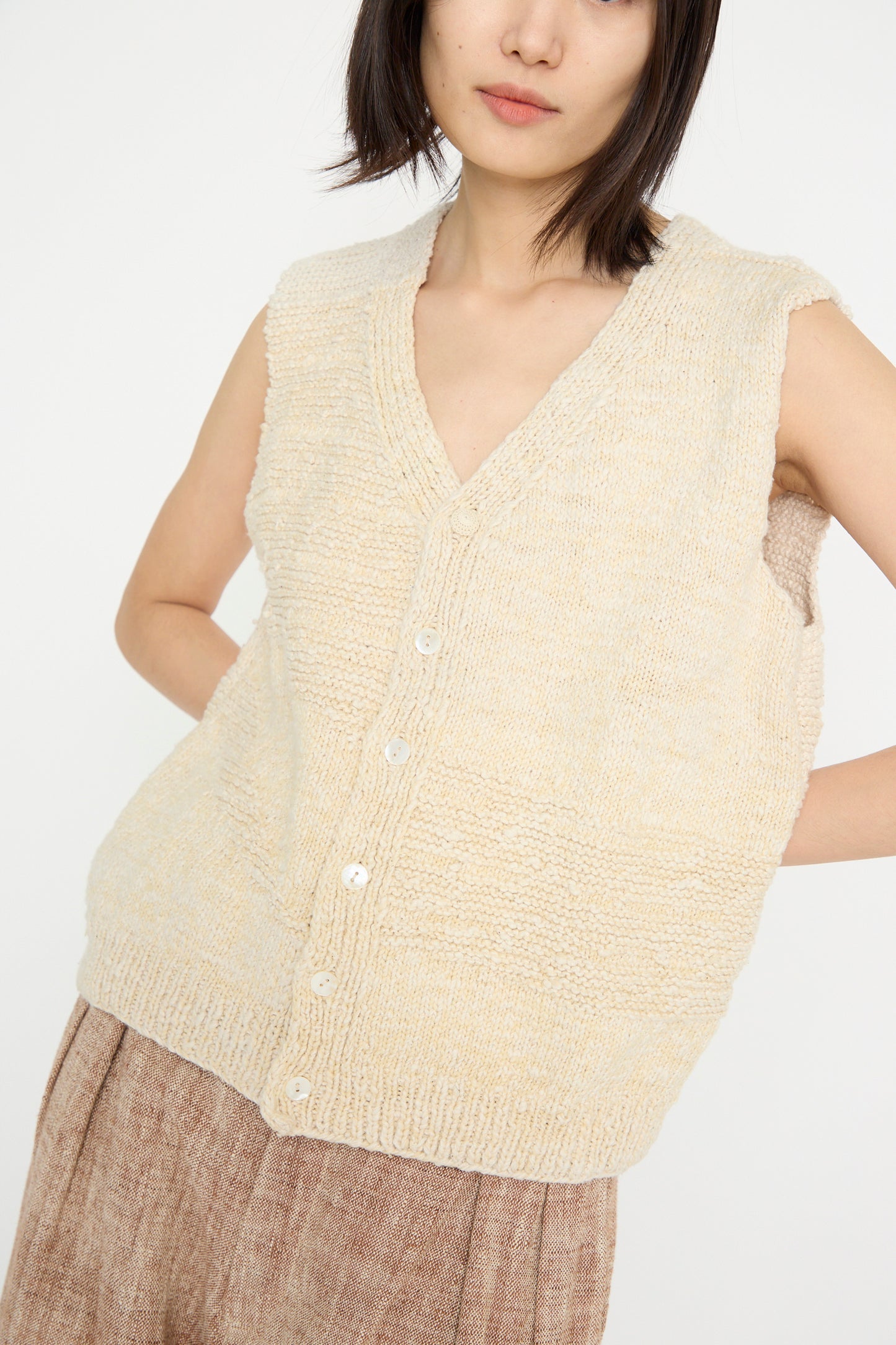 A person is posing against a white background, wearing the 11.11 Oro Vest in Ecru paired with a brown skirt.