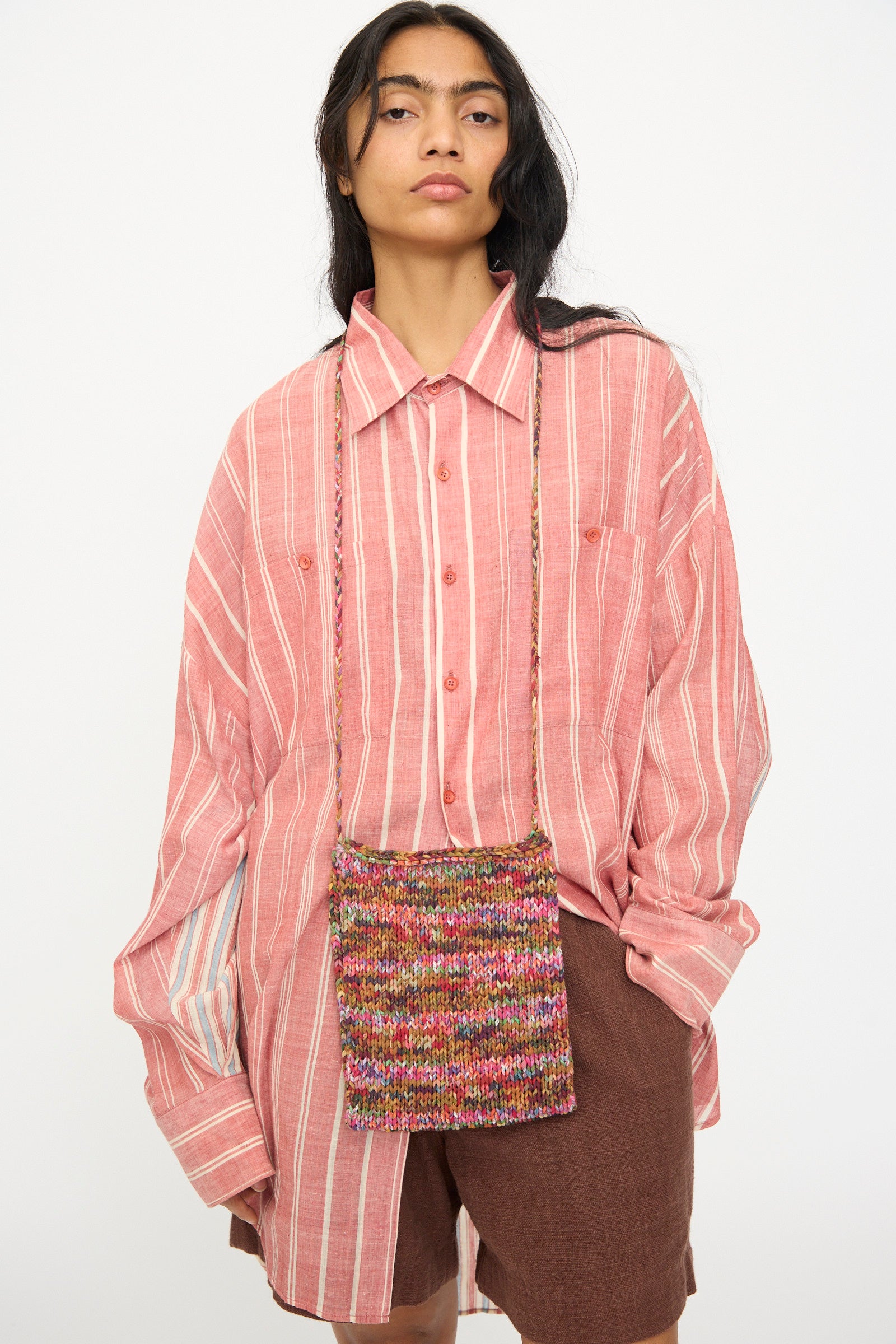 A person wearing an oversized pink striped shirt and brown shorts carries the 11.11 Silk Knitted Bag in Multi, standing against a plain white background.