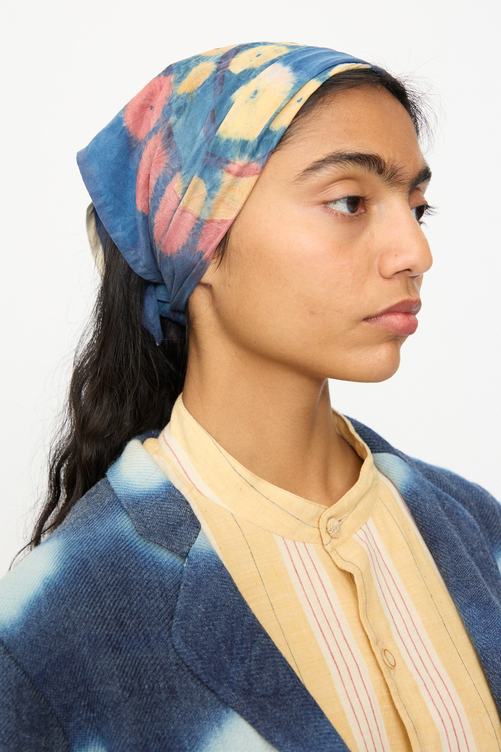 A woman wearing the 11.11 Silk Scarf in Indigo, a yellow and red striped shirt, and a blue tie-dye jacket.