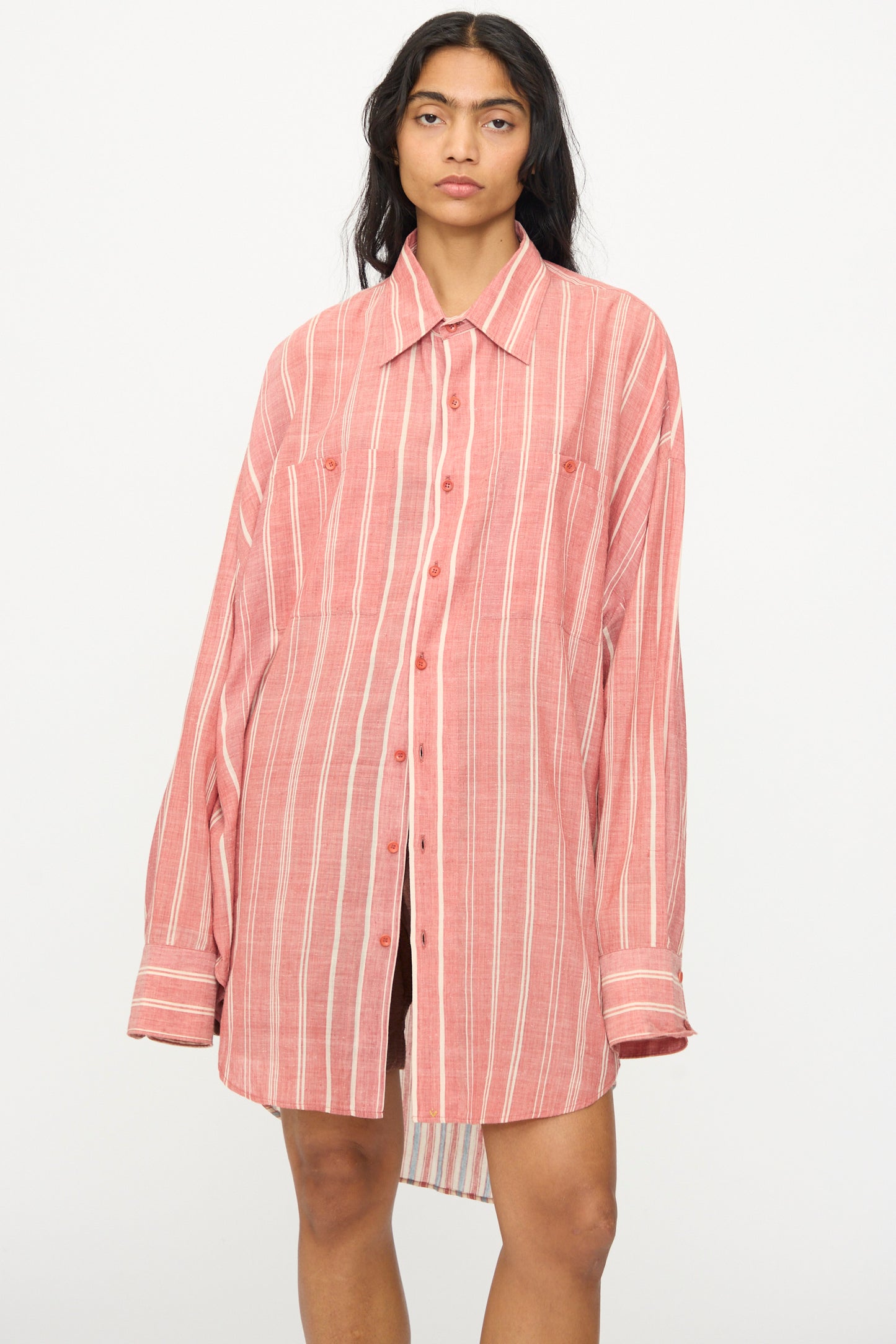 A person wearing the 11.11 Cotton Stripe Shirt in Multi, an oversized red and white striped button up made in India, stands against a plain white background.