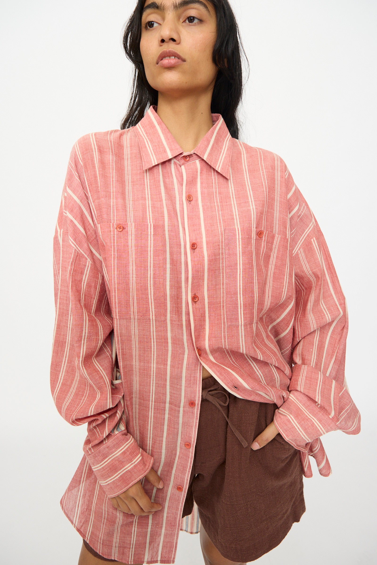A person wears the 11.11 Cotton Stripe Shirt in Multi, an oversized cotton button-up made in India, paired with brown shorts and stands against a plain background.