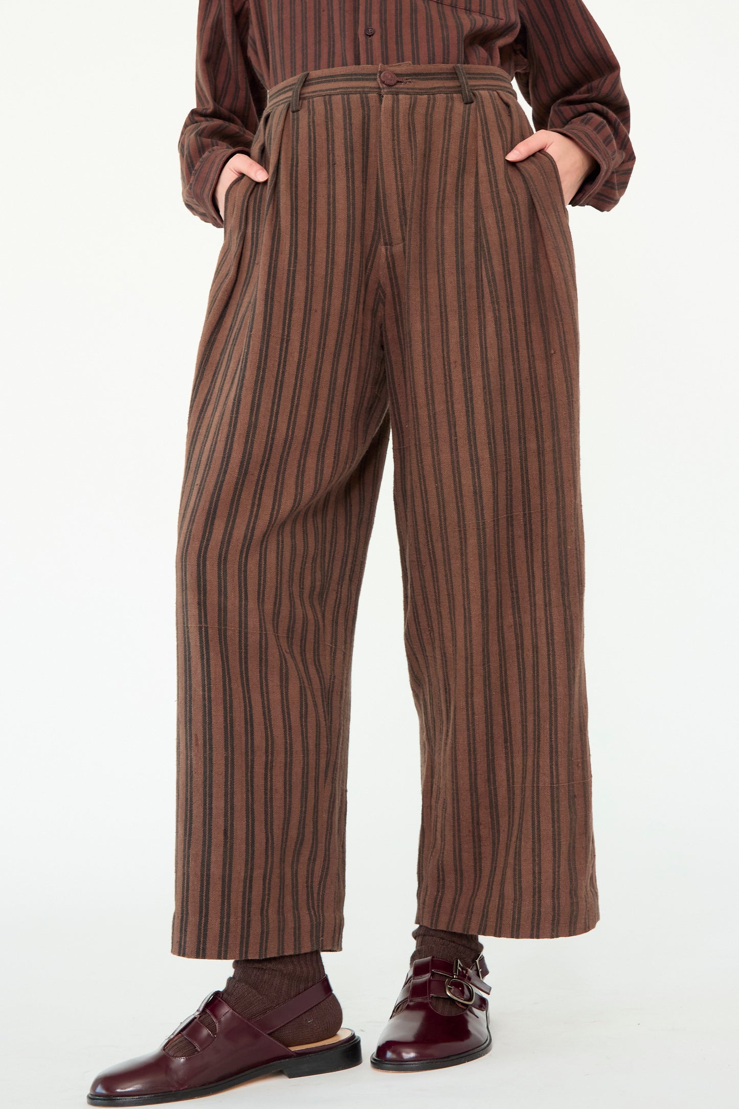 Wearing the Tel Trouser in Burnt Umber Stripe by 11.11, made from naturally dyed cotton, along with a matching long-sleeve shirt and burgundy shoes.