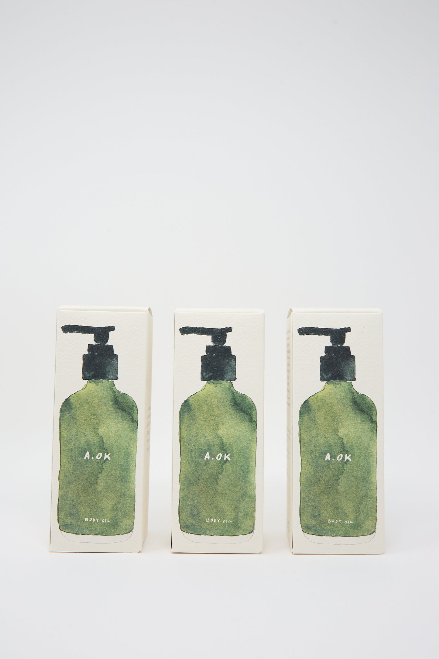 Three green pump bottles labeled "A.OK" are shown in a row against a plain white background, each containing Botanical Body Oil with a refreshing unisex aroma.