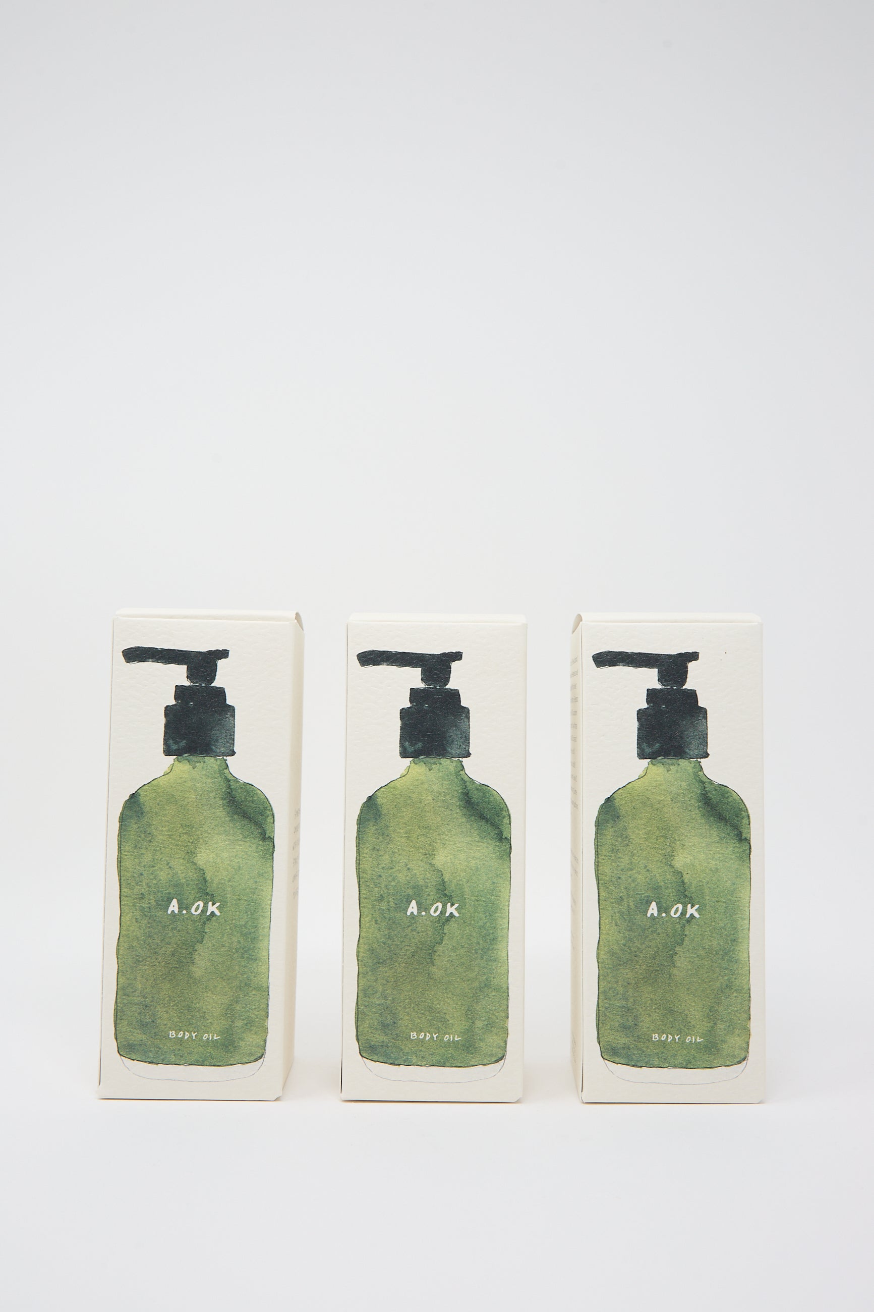 Three green pump bottles labeled "A.OK" are shown in a row against a plain white background, each containing Botanical Body Oil with a refreshing unisex aroma.