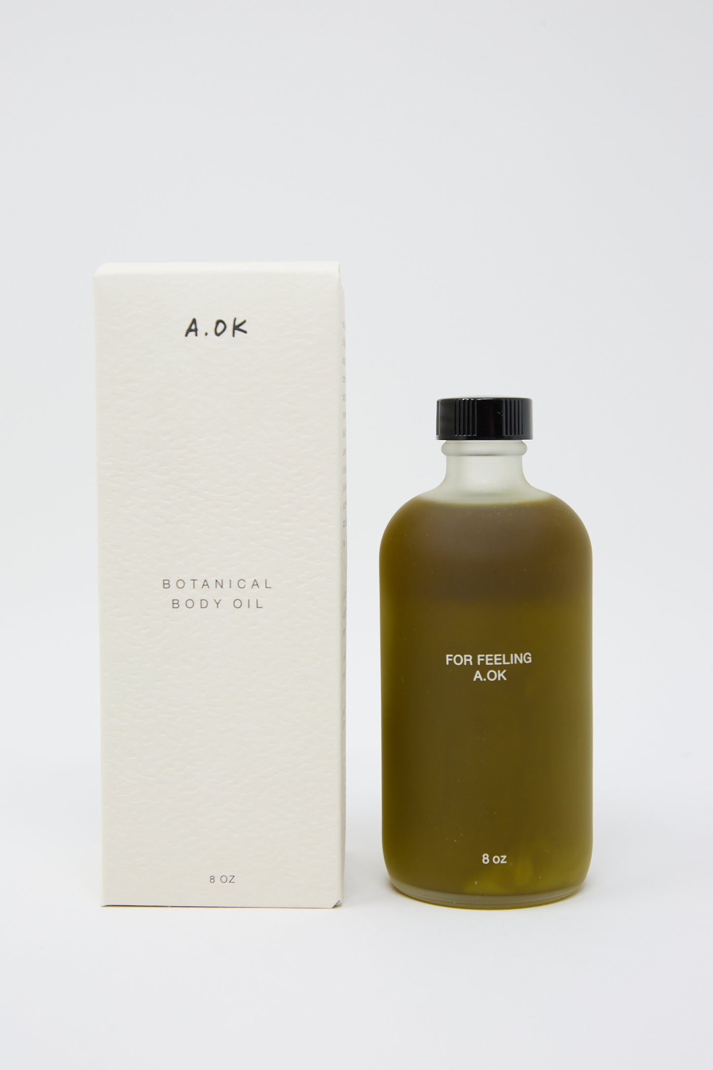 A bottle of A.OK Botanical Body Oil, 8 oz, with its unisex aroma, is shown next to its white packaging box.
