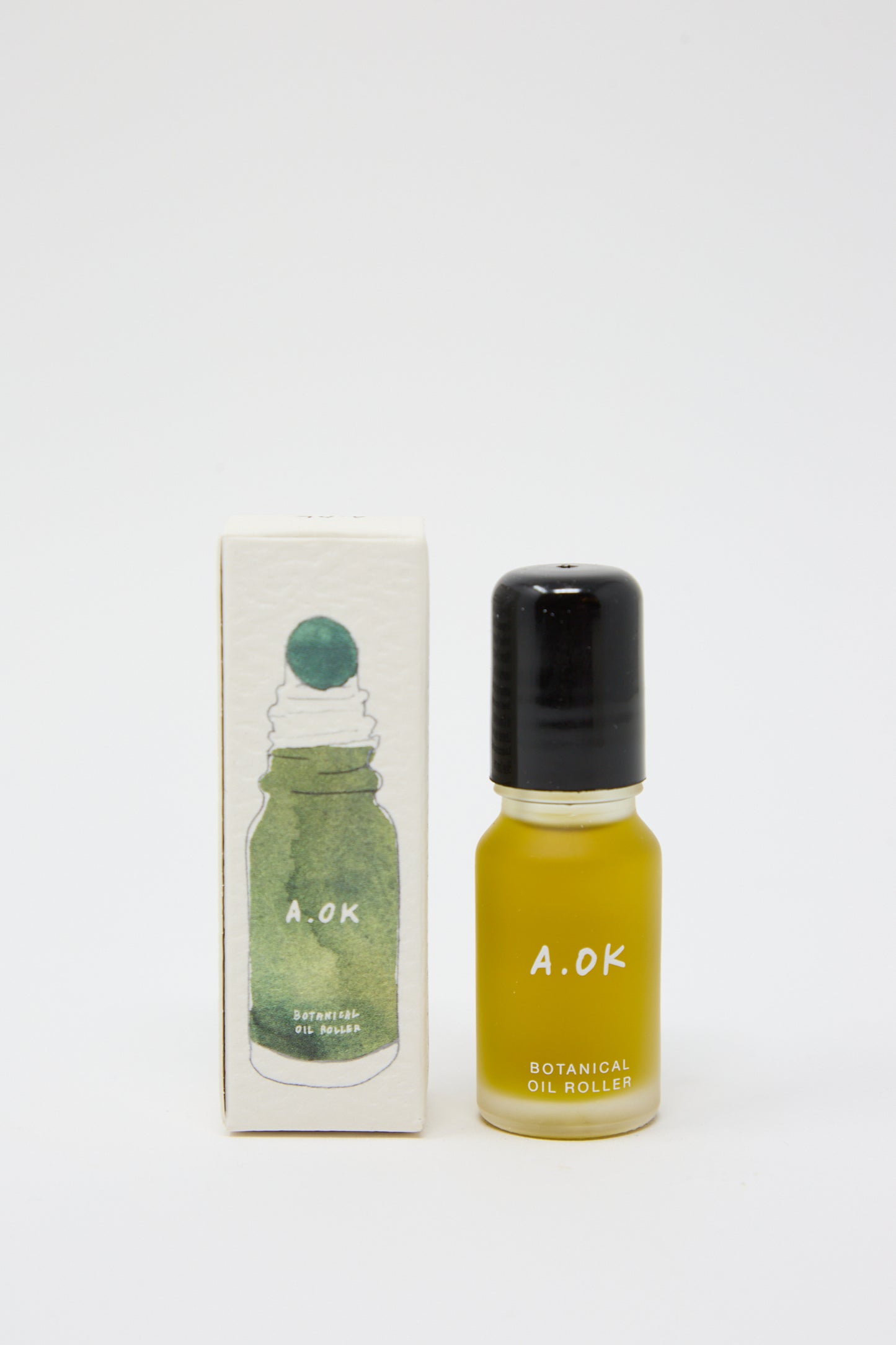 A small bottle of Botanical Oil Roller labeled "A.OK," infused with natural blood orange, is positioned next to its white box packaging featuring a green illustration of the product. Its travel-friendly size makes it perfect for on-the-go use.