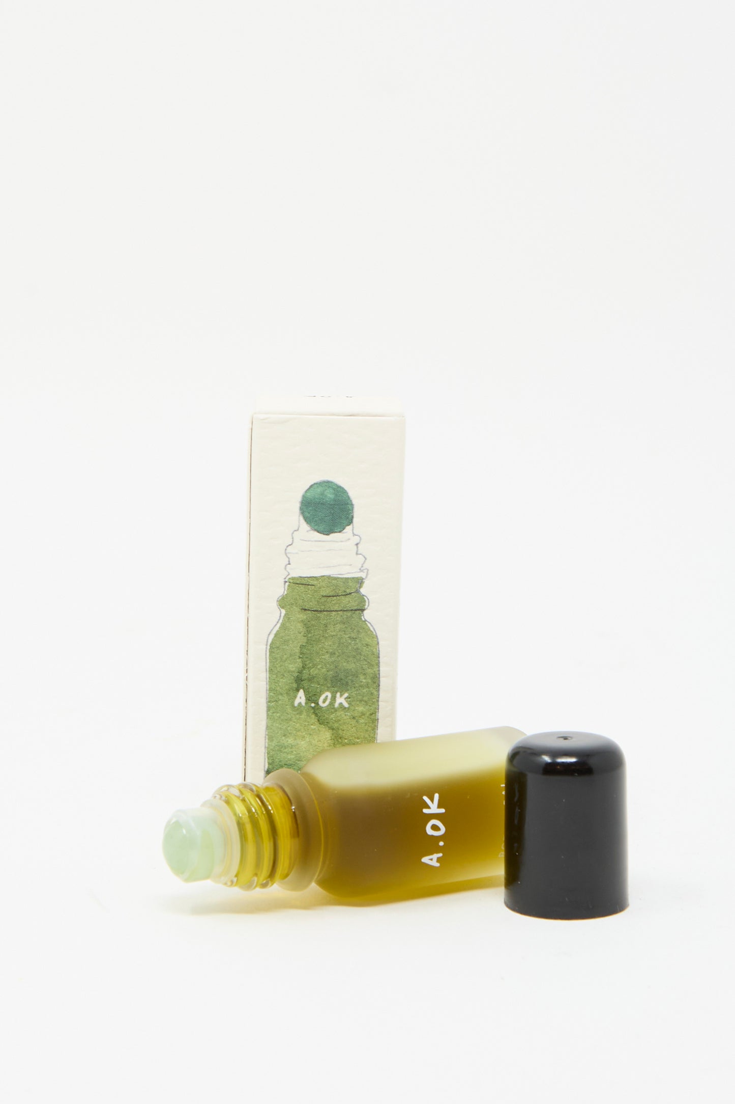 A small bottle of A.OK's Botanical Oil Roller with a black cap is shown next to its packaging, featuring a green bottle illustration on a white background. Infused with calming lavender essence, this roller is your ideal companion for a serene skincare routine.