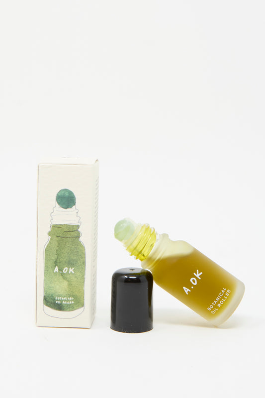 A small glass bottle labeled "Botanical Oil Roller" by A.OK lies beside its box, which showcases an illustration of a similar bottle. The black cap is removed to reveal lavender-infused soothing contents.