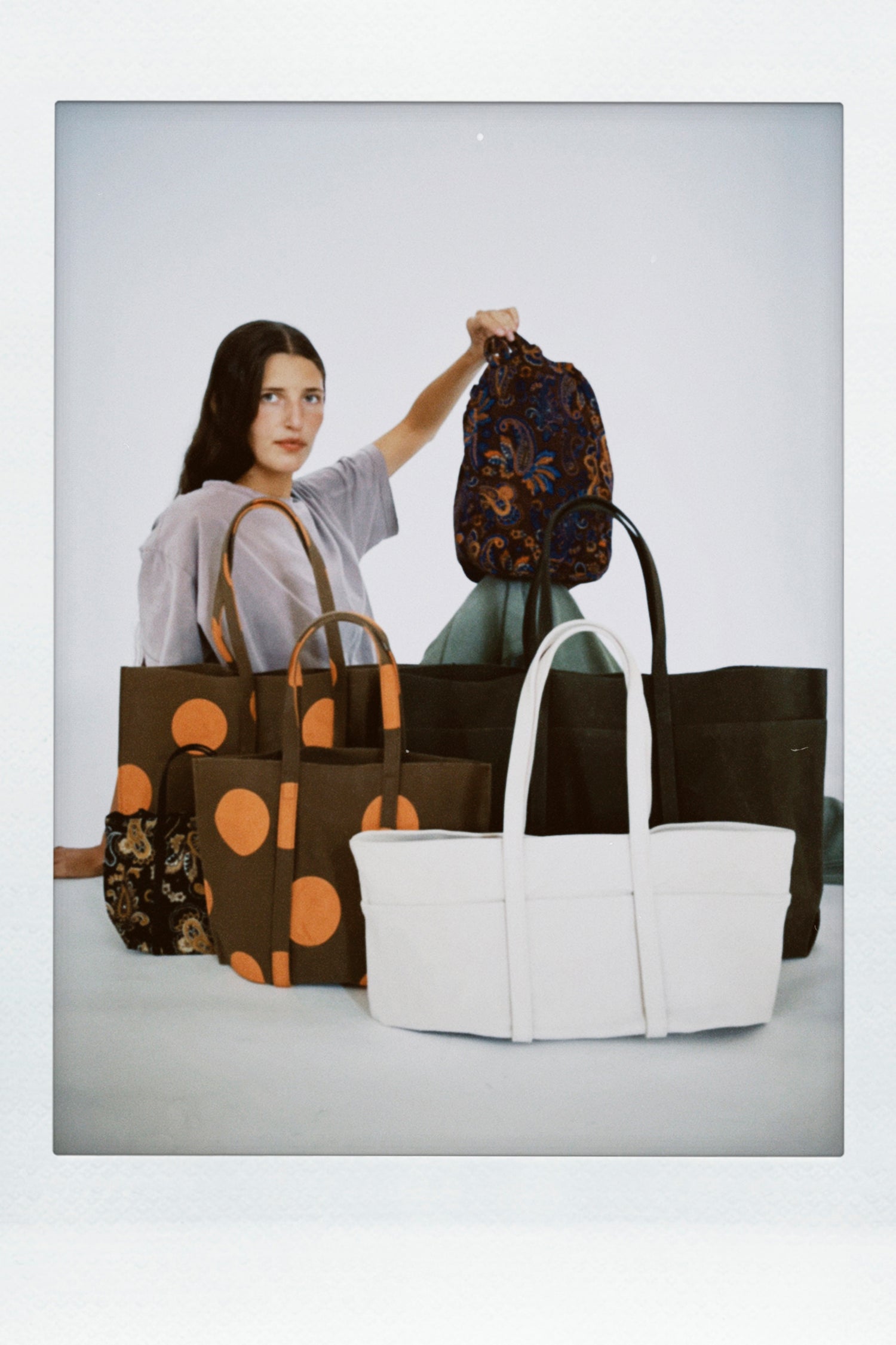 A woman sits behind a group of tote bags from Amiacalva.