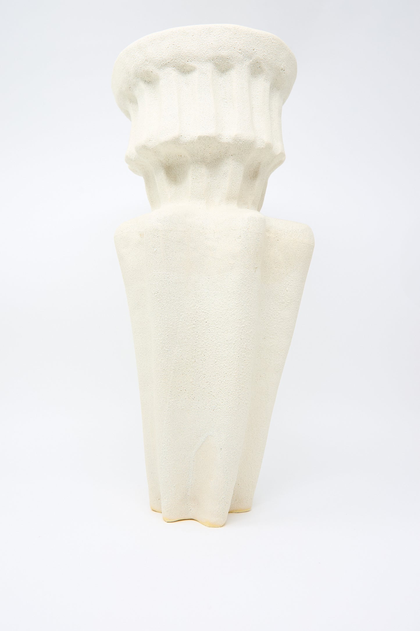 The Column Vessel in White, by ANK Ceramics, is a beige-textured vase made from white stoneware. It showcases a fluted design with a tiered neck and is set against a plain background.