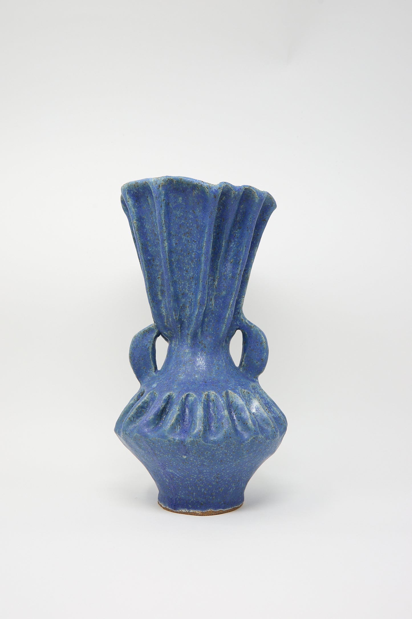 The Pleat Vase with Handles in Blue by ANK Ceramics is a figurative stoneware creation featuring a ruffled top and two handles, all beautifully accented with a shimmering blue glaze on a plain white background.