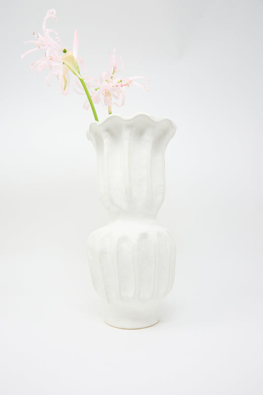 A single stem of light pink flowers stands out against a plain background in the Pleat Vase from ANK Ceramics, featuring a matte white glaze and an eye-catching wavy design.