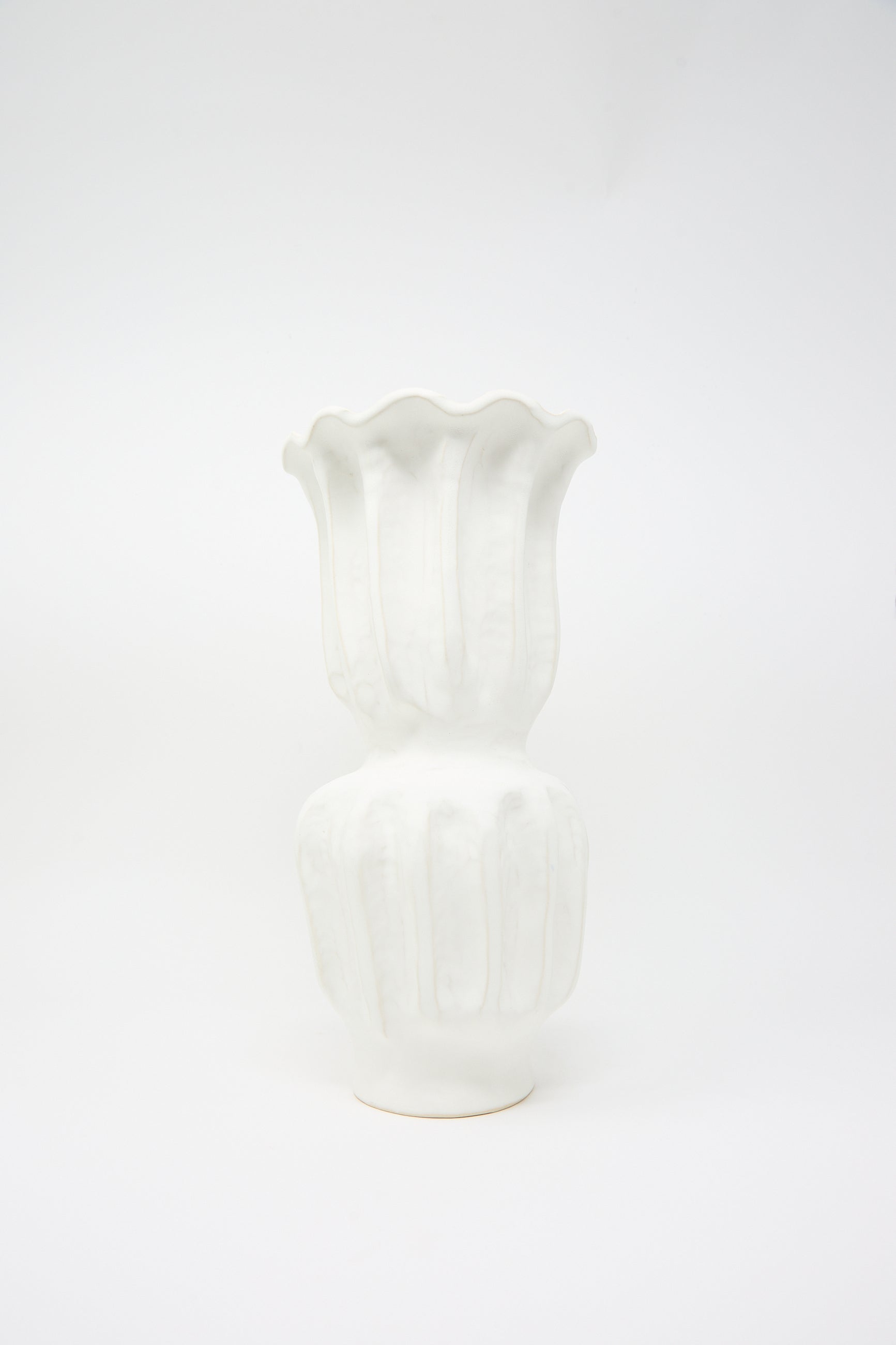 The Pleat Vase in Matte White Glaze from ANK Ceramics beautifully showcases a matte white finish that accentuates its rippled top and bulbous base, crafted from white stoneware and set against a plain background.