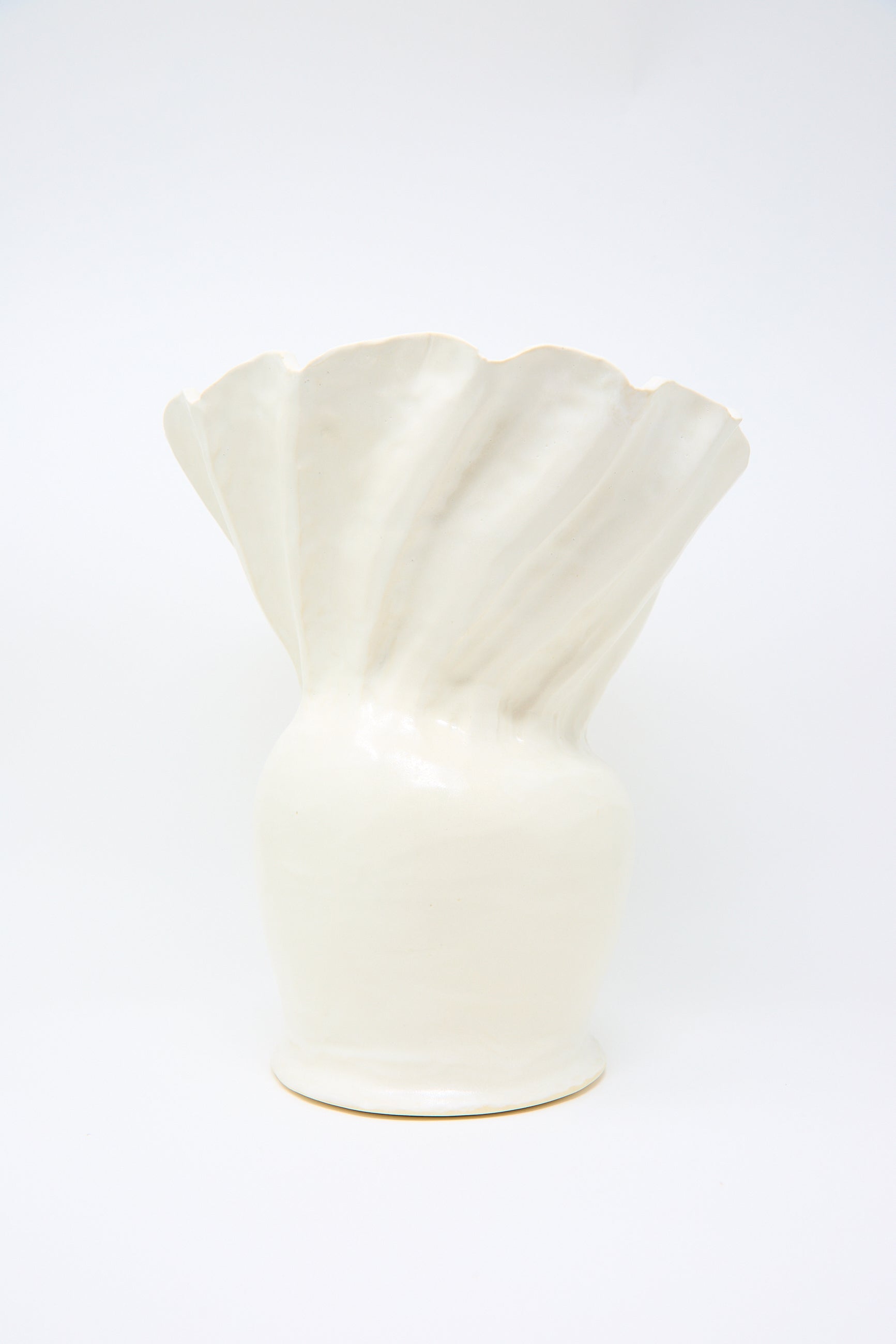 The Pleat Vase in White by ANK Ceramics features a wavy, flared top reminiscent of a seashell, elegantly finished in a satin white glaze against a plain white backdrop.