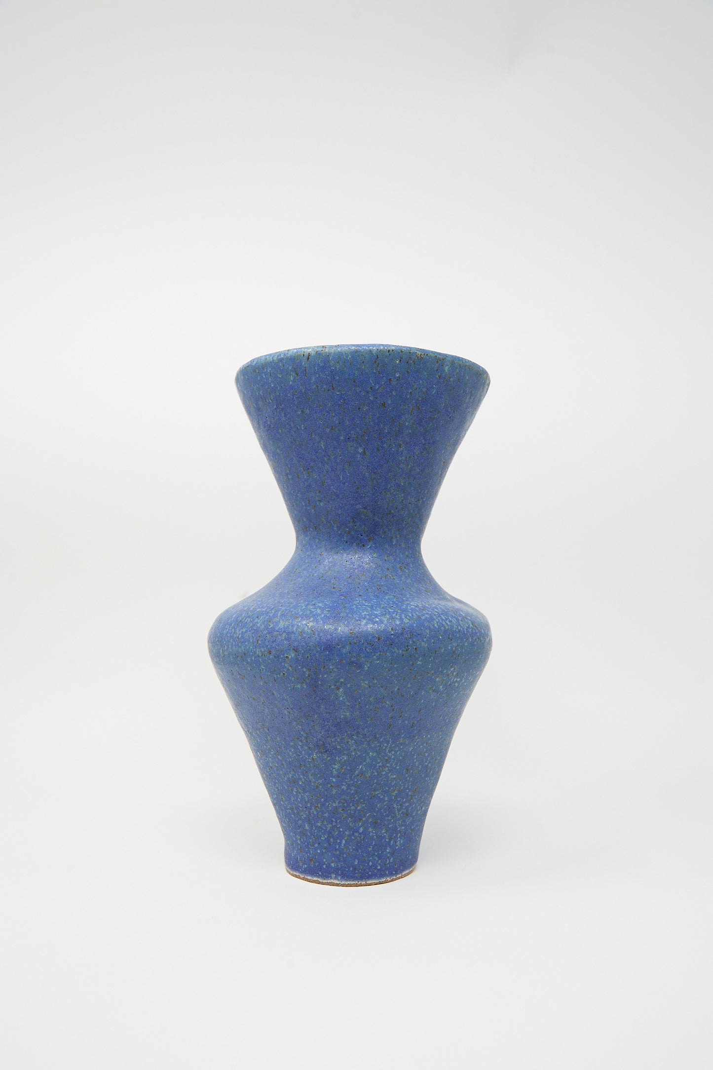 The "Vase in Blue" by ANK Ceramics is an hourglass-shaped stoneware piece featuring a textured surface and vibrant blue glaze, beautifully displayed against a plain white background.