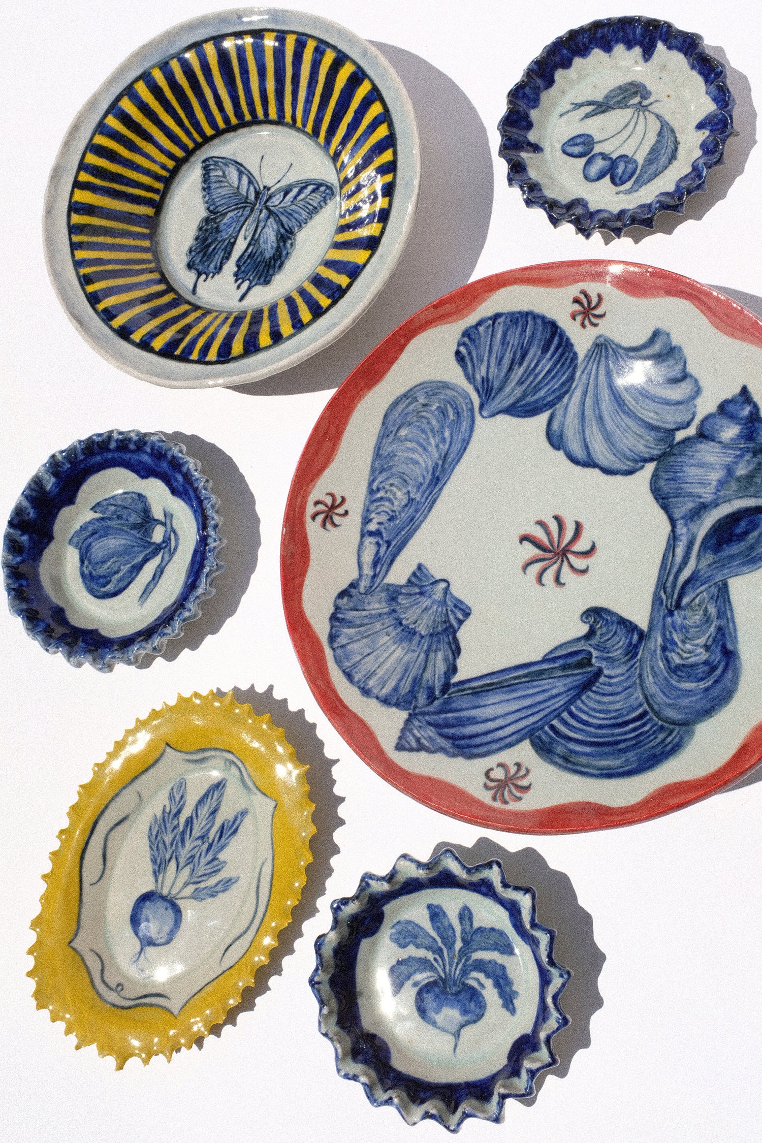 An image of hand-painted ceramics in yellow, blue, and red from Ariel Clute, in the sunlight on a white background.
