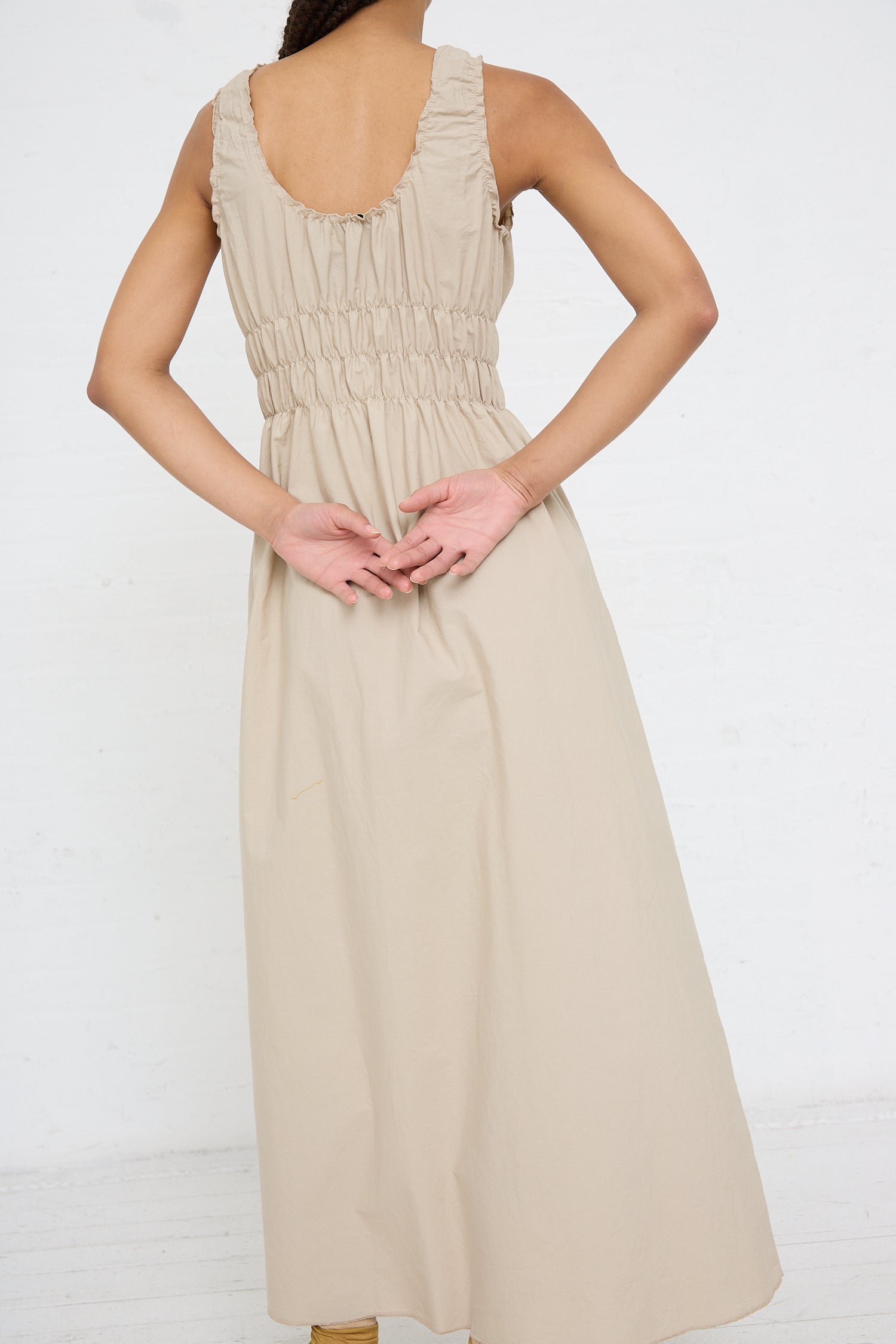 Woman standing with her back to the camera, wearing a AVN Accordion Dress in Beige with ruched detailing, crafted from lightweight cotton.