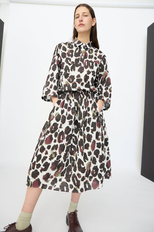 A woman stands with hands in pockets, wearing the AVN Bloom Skirt in White with Print, green socks, and brown shoes against a plain white background.