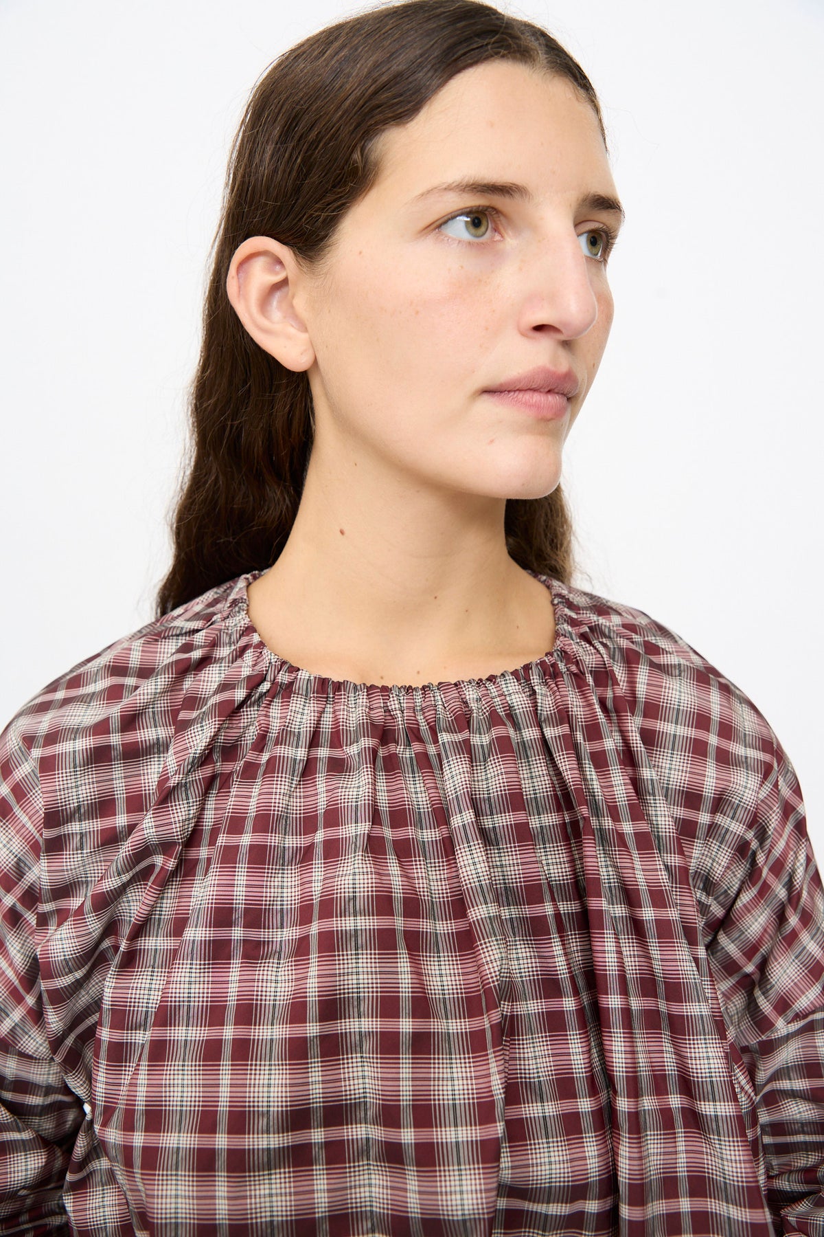Woman wearing a Bolla Shirt in Bordeaux Check, featuring a boxy fit, burgundy and white bordeaux check pattern, and a gathered, round neckline.