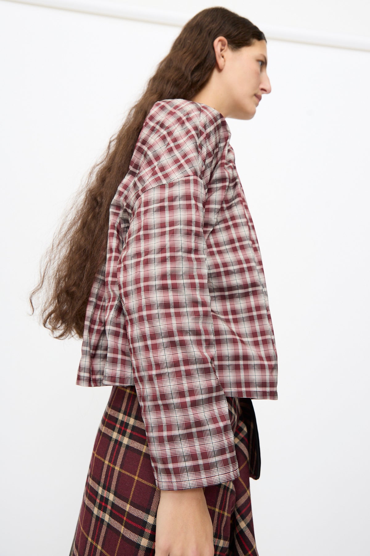 A person wearing a Bolla Shirt in Bordeaux Check in a boxy fit, red and white plaid, paired with a dark bordeaux check skirt.