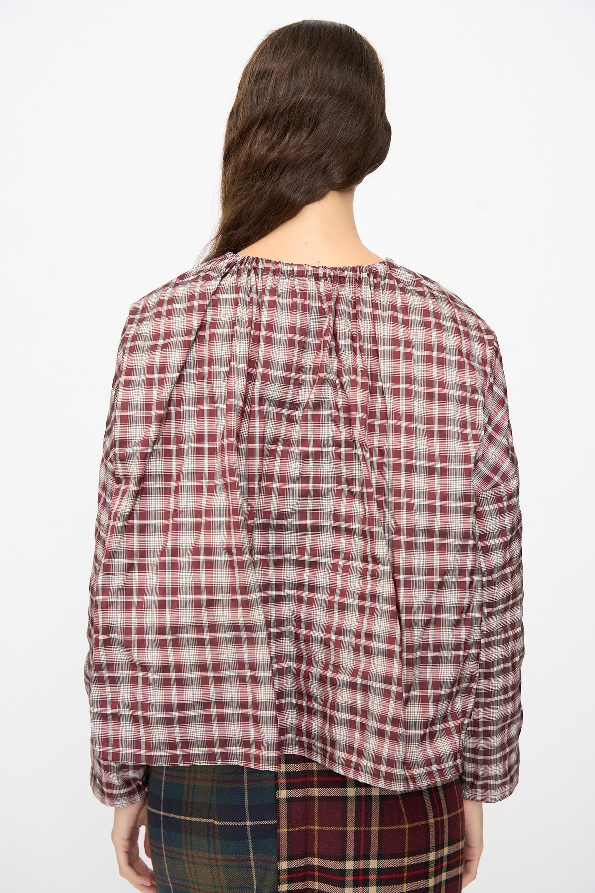 Back view of a person wearing a boxy-fit Bolla Shirt in Bordeaux Check paired with a contrasting green and burgundy plaid skirt.