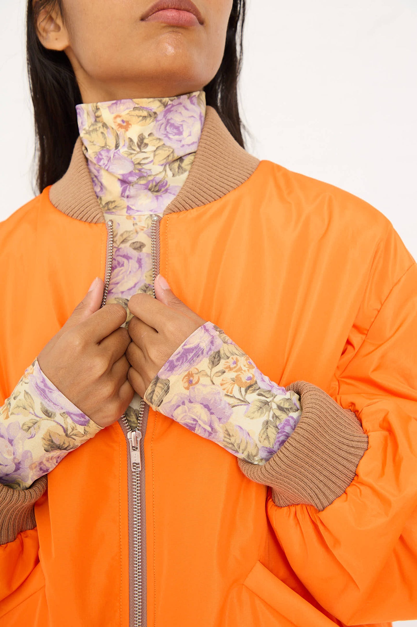 A person wearing the AVN Bomber Jacket in Orange unzips it slightly, revealing a floral-patterned inner layer and matching cuffs.