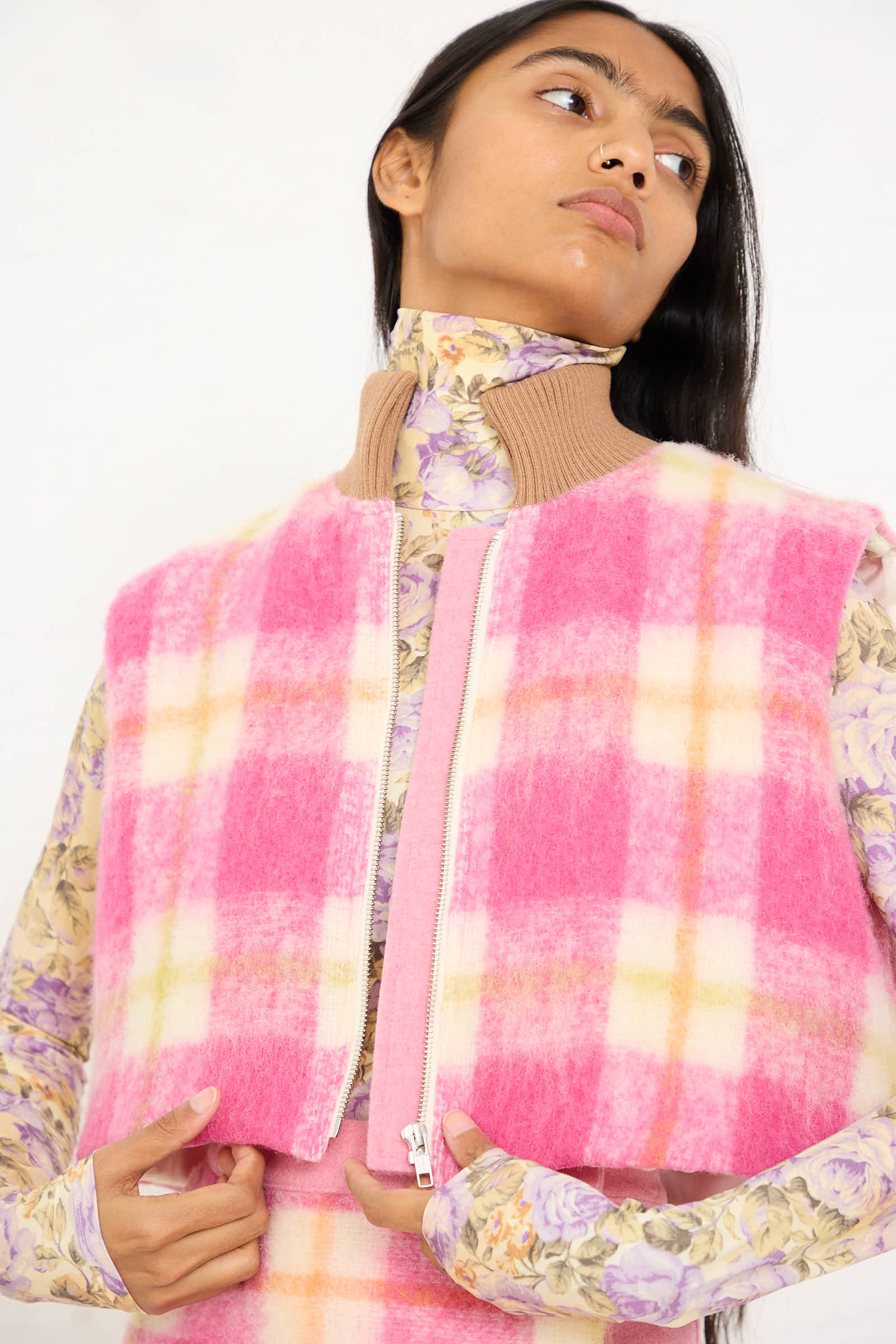 A person is wearing the Cool Bomber Jacket in White, Pink, and Green Check by AVN over a floral turtleneck. They are looking slightly upwards and to the side.