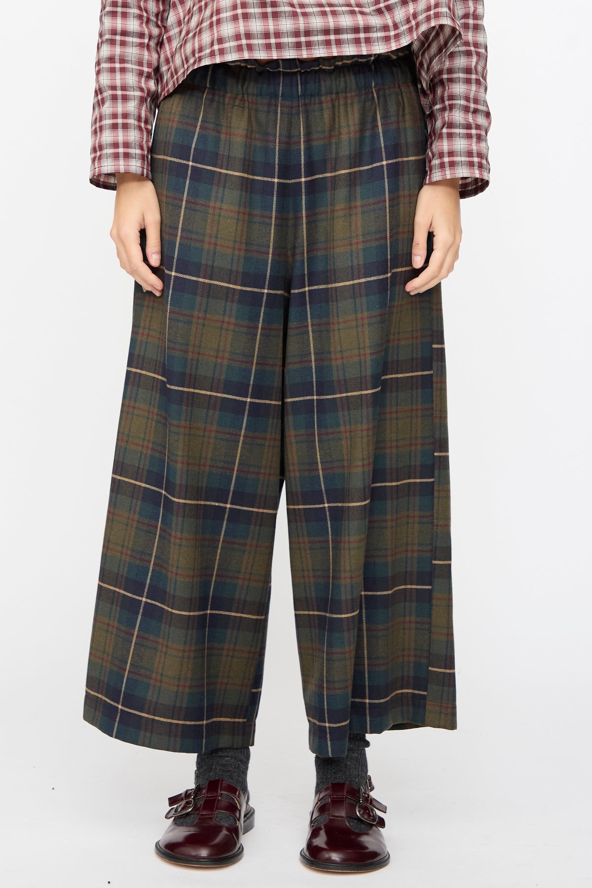AVN Easy Pants in Military Check featuring a wide-leg dark green and navy plaid pattern, paired with a maroon plaid shirt and dark buckle shoes.
