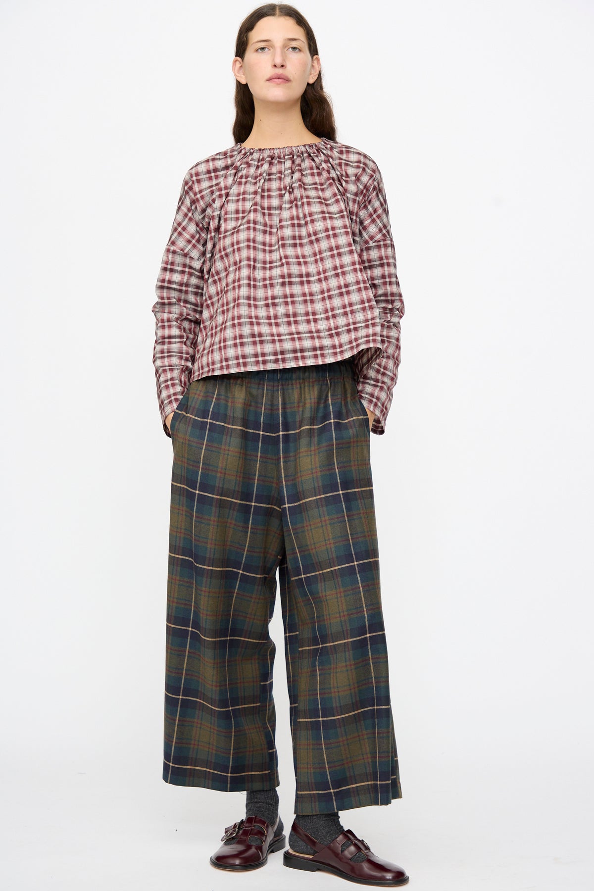 A person wearing a long-sleeved plaid blouse, AVN Easy Pants in Military Check, and dark loafers.