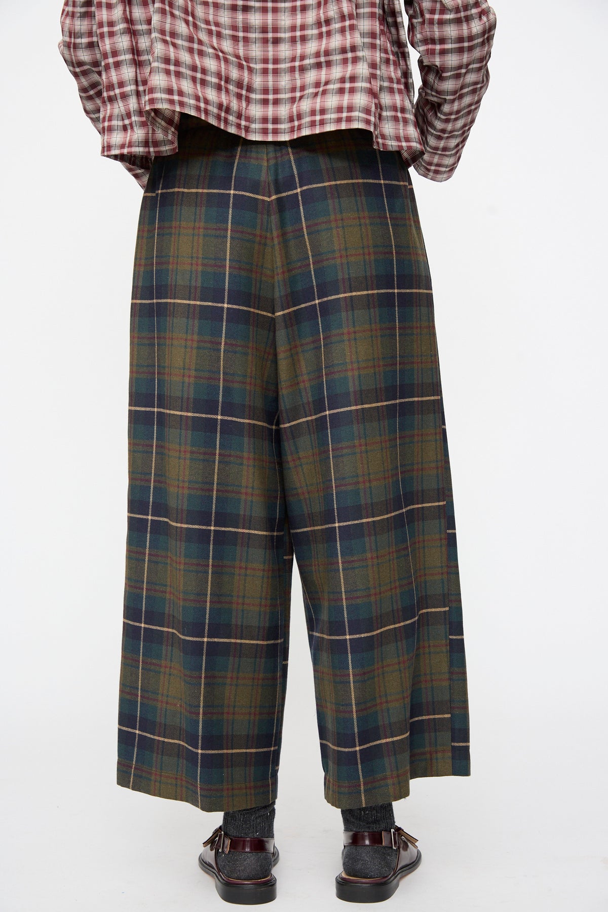 Backside of the AVN Easy Pants in Military Check: wide-leg, dark green wool trousers worn with a maroon and tan plaid long-sleeve shirt.