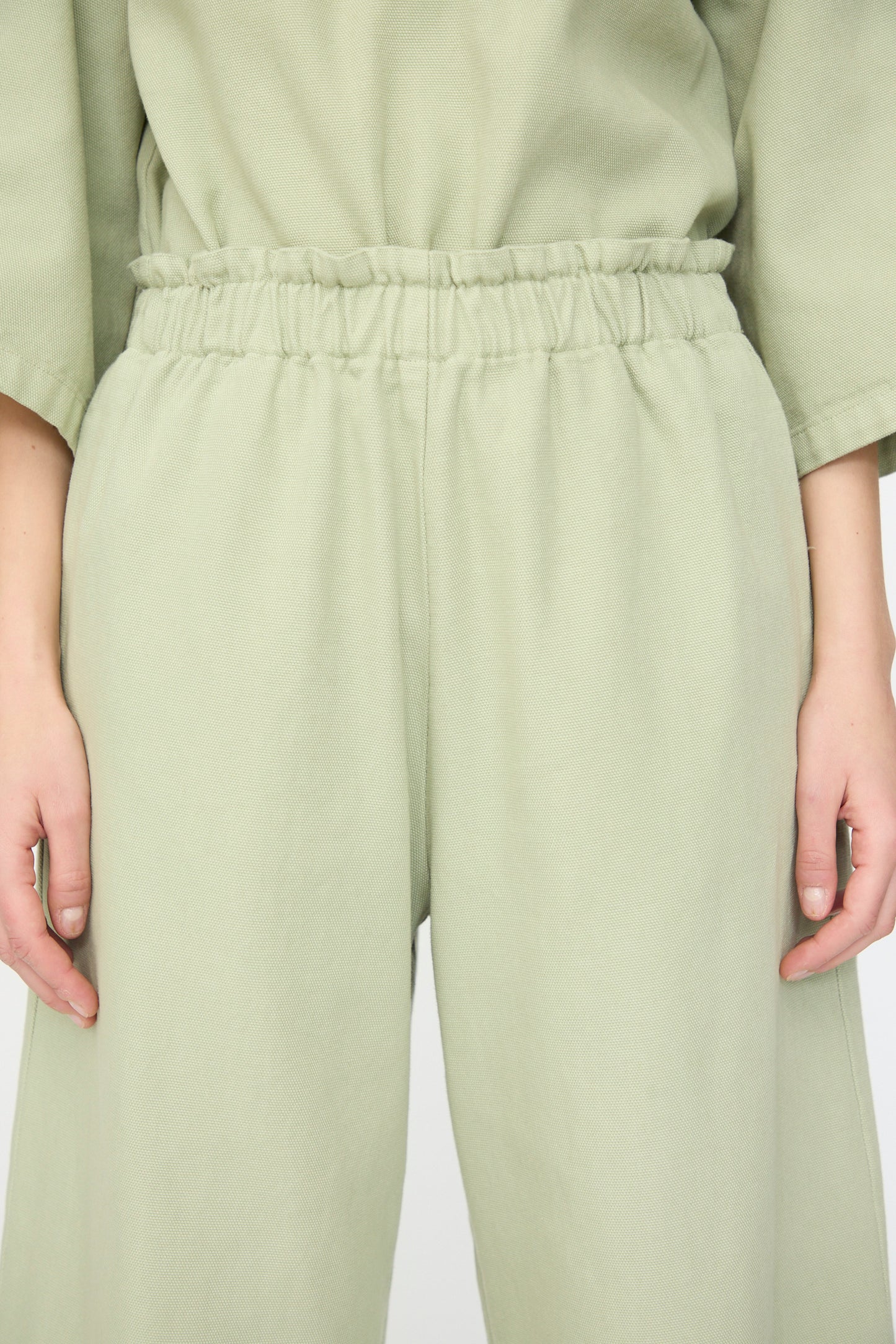 Model wears AVN’s Easy Pants in Sage, featuring a loose fit, elastic waistband, and wide-leg silhouette for comfort. Shown from waist to mid-thigh with hands relaxed at sides, styled with a matching top.