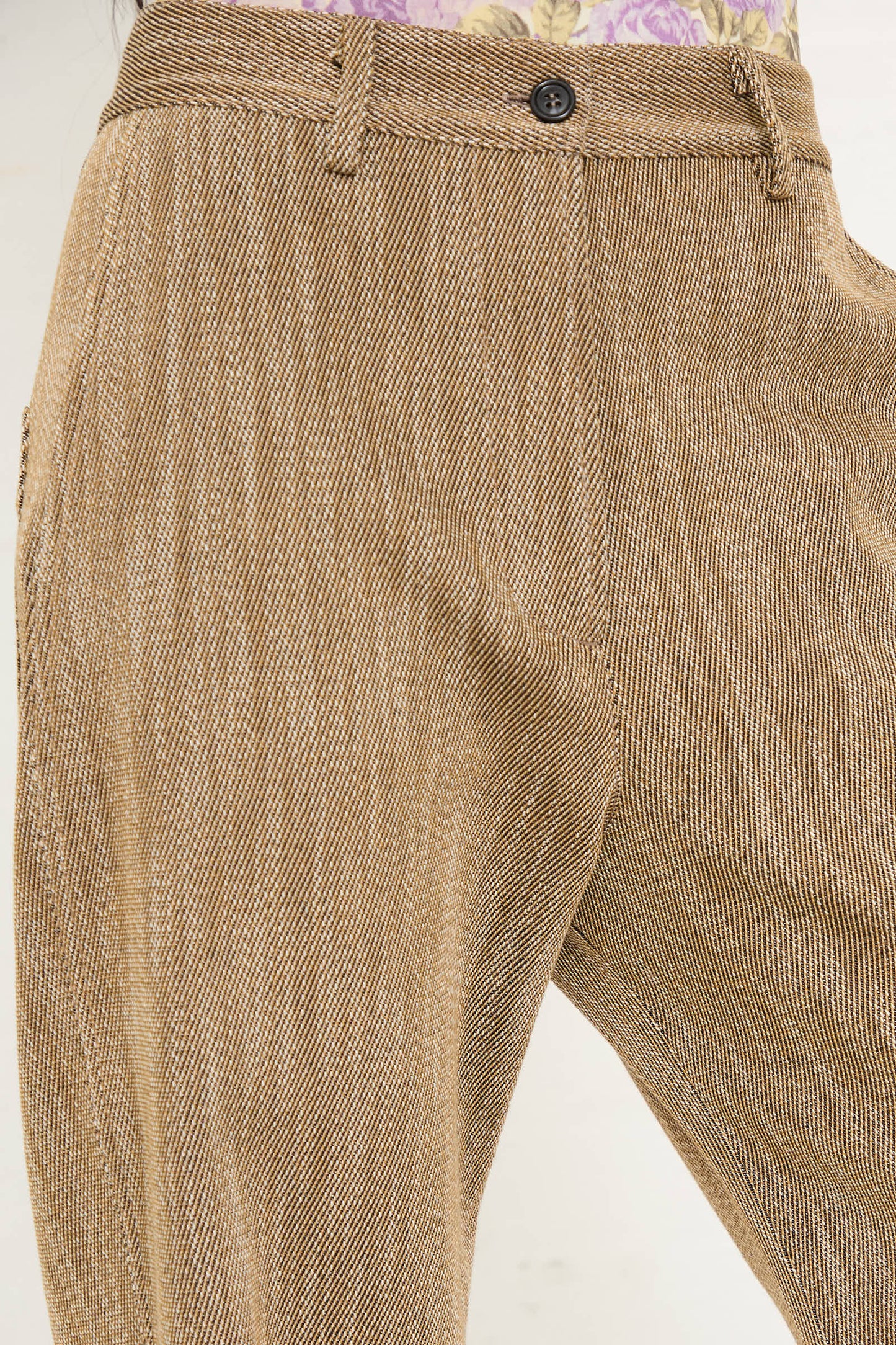 A person wearing AVN's Iris Pant in Beige, featuring a herringbone pattern and side slash pockets, with a partially visible floral shirt.