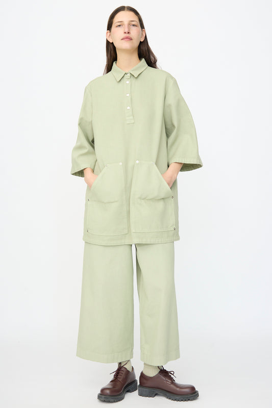 A person stands facing forward, wearing the AVN Joyeux Dress in Sage— a loose-fitting, textured cotton dress with pockets—paired with dark brown lace-up shoes.