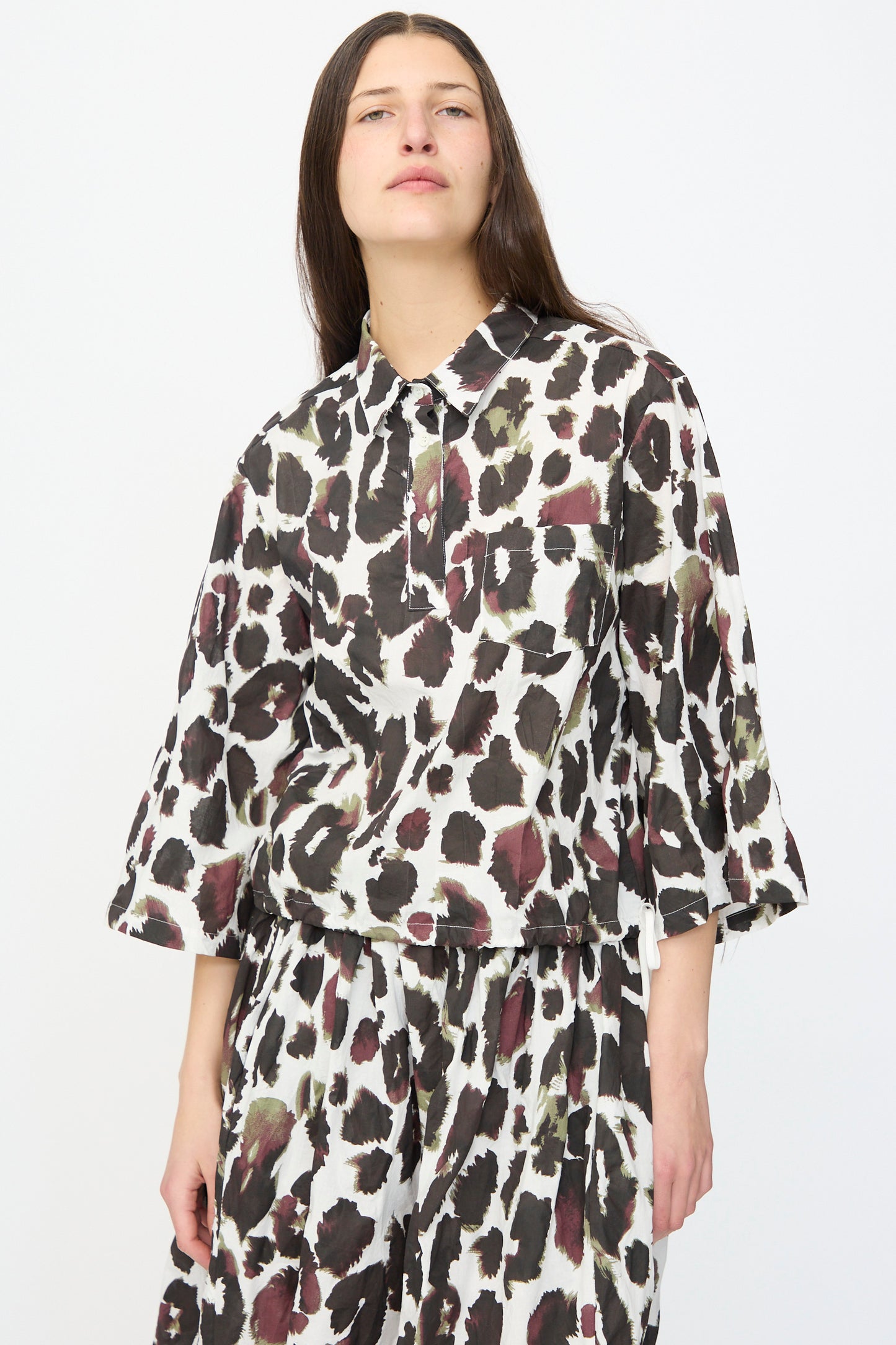 A person stands against a plain background wearing the AVN Joyeux Top in White with Print, a loose-fitting, made-in-Italy 3/4 sleeve top featuring an abstract black, brown, and white spotted pattern.