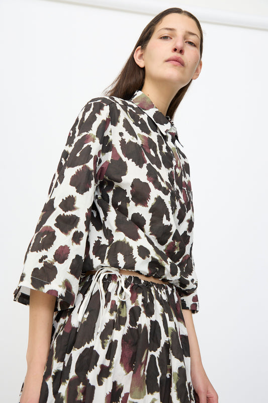 A person wears the AVN Joyeux Top in White with Print, a loose-fitting, 3/4 sleeve cotton top featuring a black and brown abstract spotted pattern, paired with a matching skirt, standing against a plain white background.