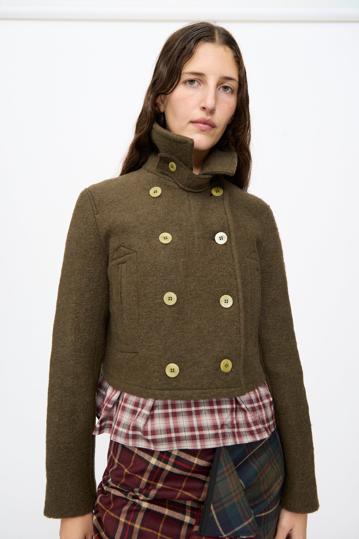 A person wears a cropped, olive Mini Peacoat in Khaki with a high collar over a plaid shirt.