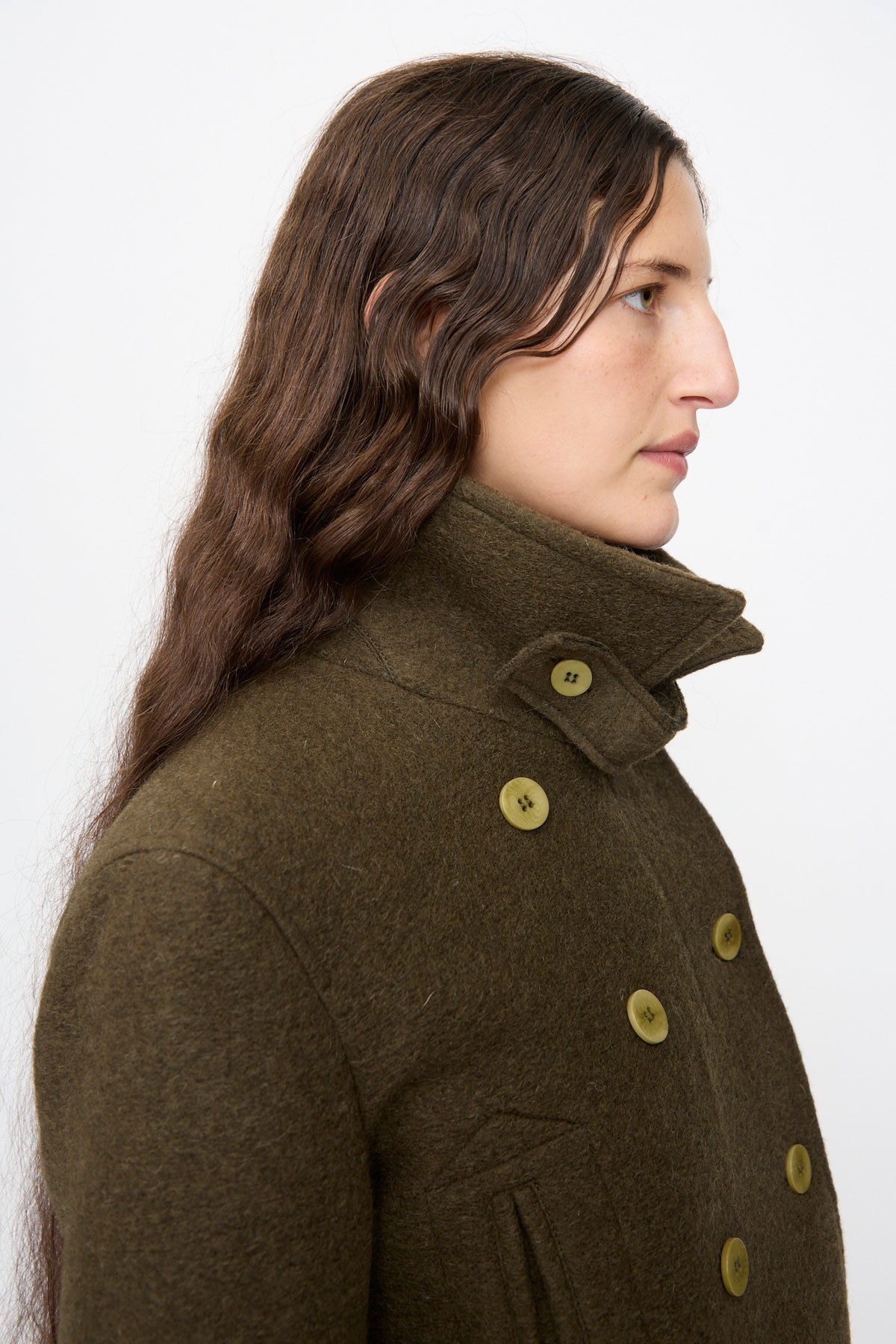 Profile view of a person wearing a dark olive green, cropped-fit wool-blend Mini Peacoat with a high collar.