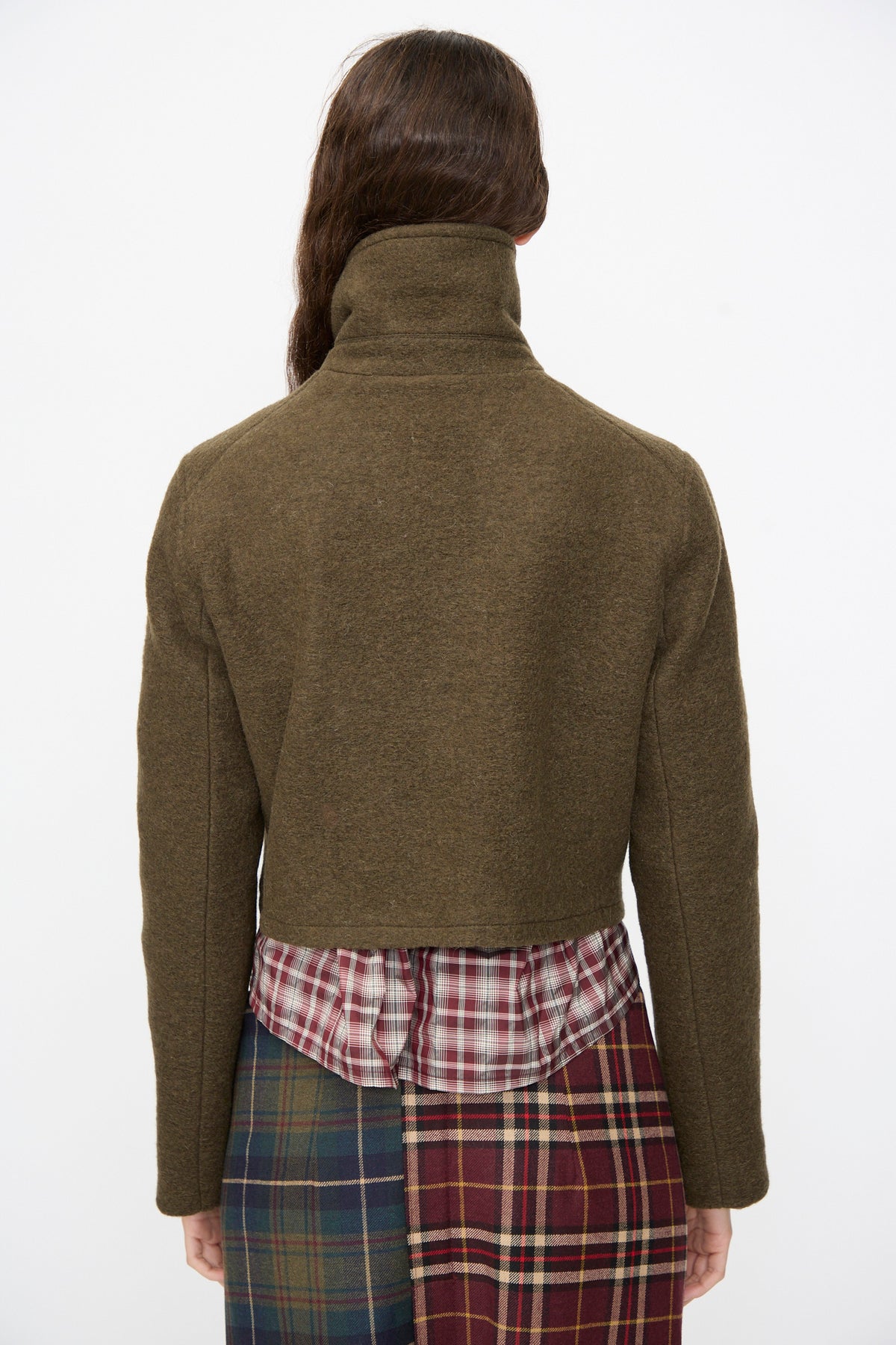Back view of a cropped olive green Mini Peacoat in Khaki over a plaid shirt and plaid skirt.