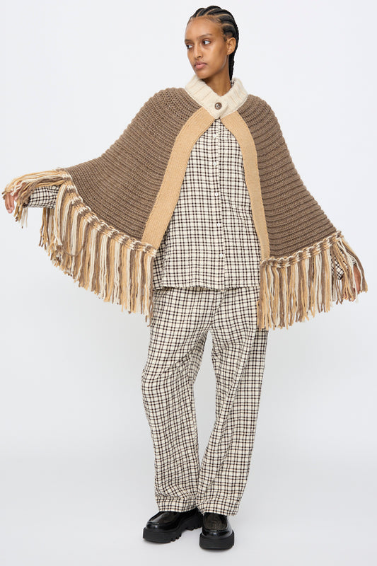 A person wearing the AVN Peru Poncho in Brown and Beige Placket stands against a plain white background, styled over a plaid shirt, pants, and black shoes.