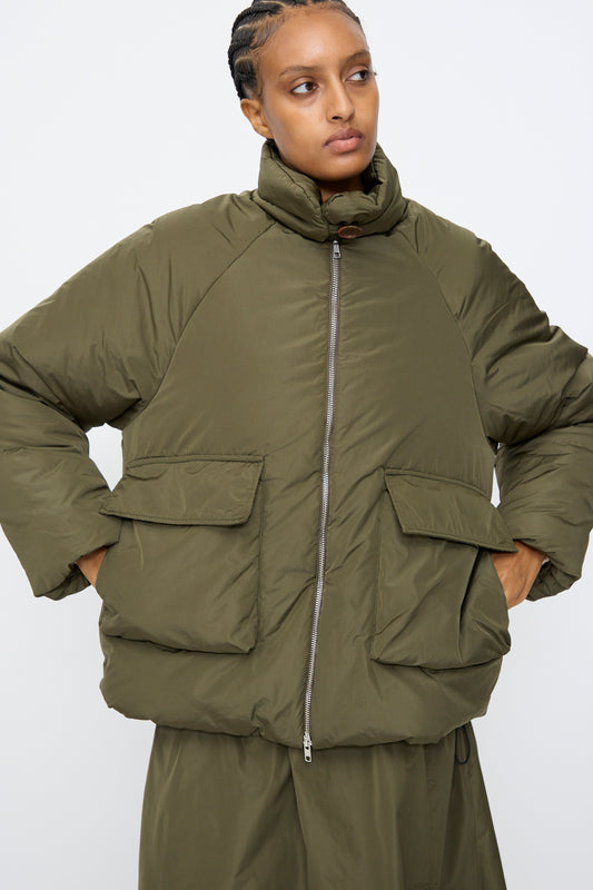 A person wearing the AVN Piumino Jacket in military green, featuring an oversized fit, large front pockets, and a high collar, stands against a plain background.